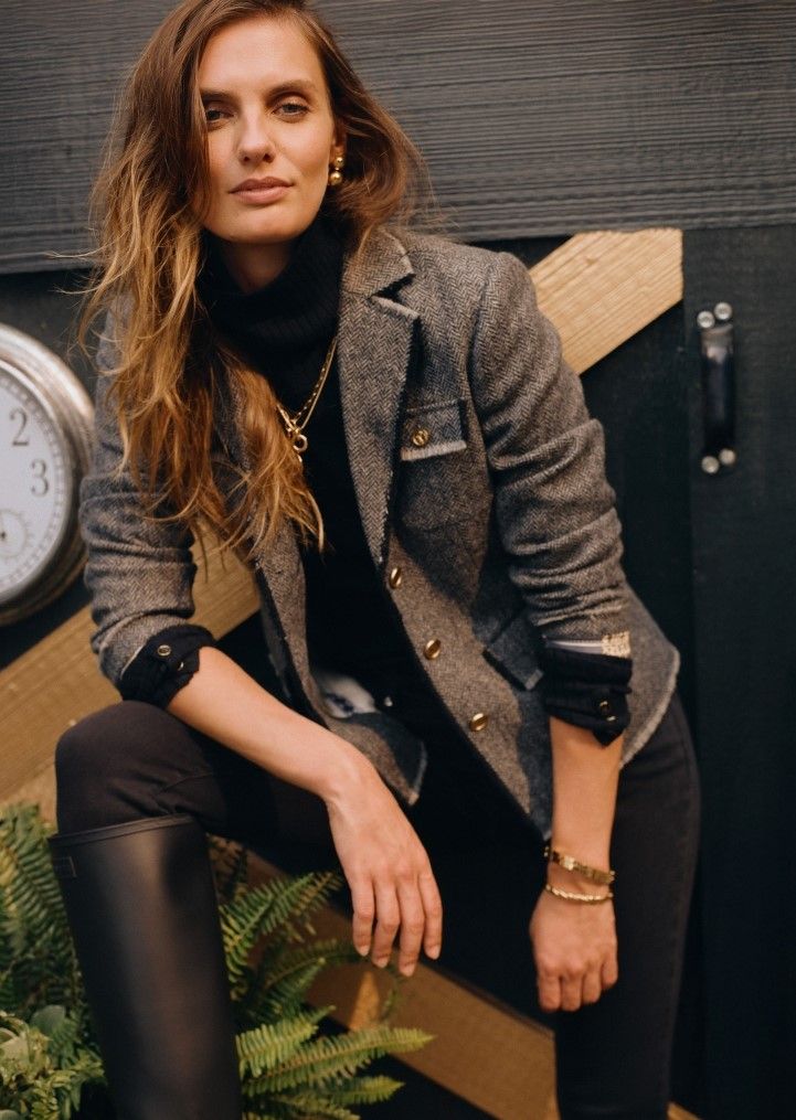 woman leaning away from barn door wearing gray herringbone jacket with black turtleneck