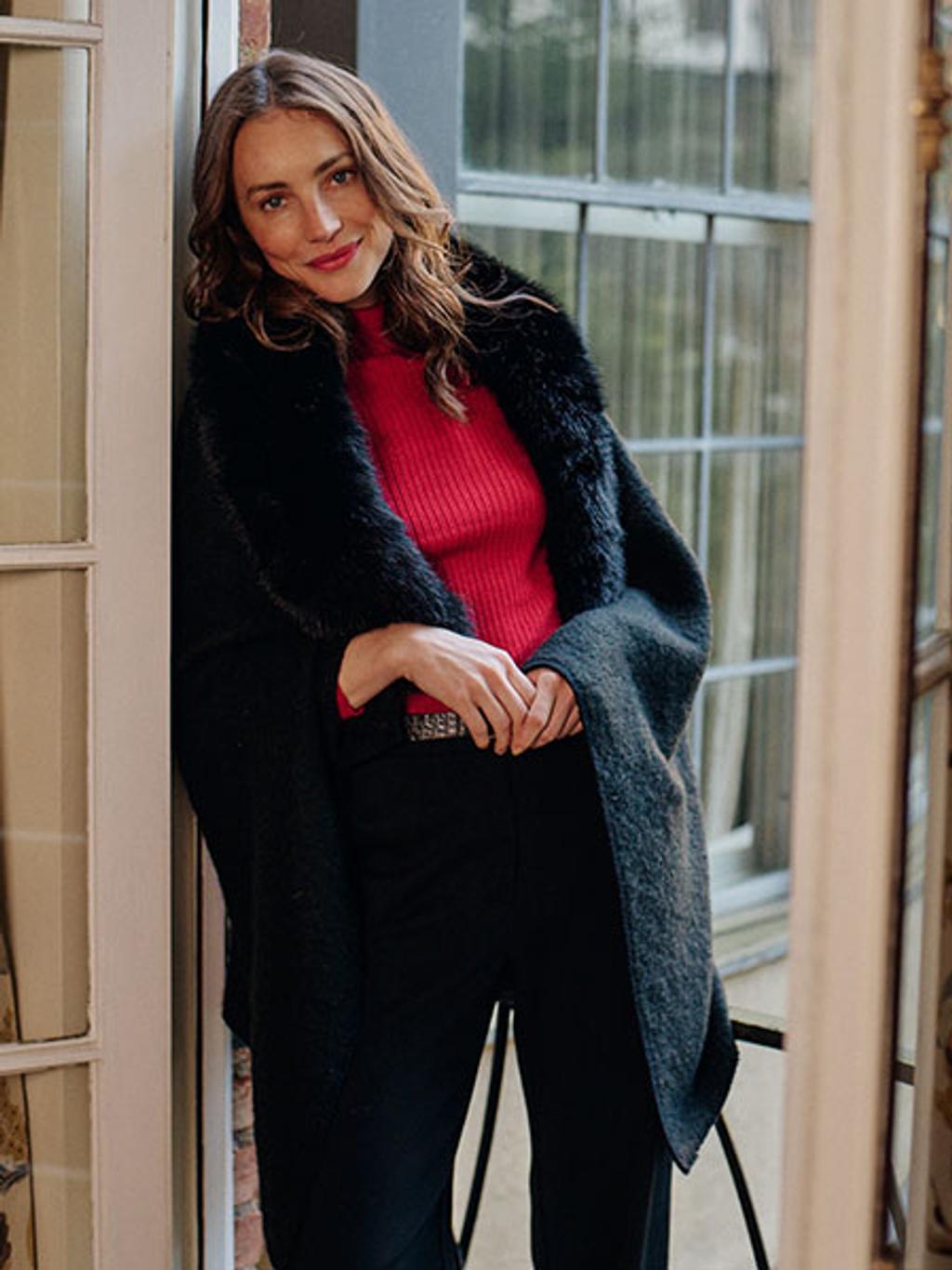Model wearing poncho, rib-knit turtleneck, and pants on a balcony Model wearing poncho, rib-knit turtleneck, and pants on a balcony