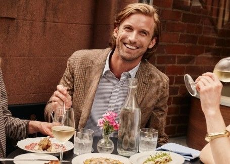 man sitting outside at cafe wearing brown houndstooth sport coat over blue and white striped shirt