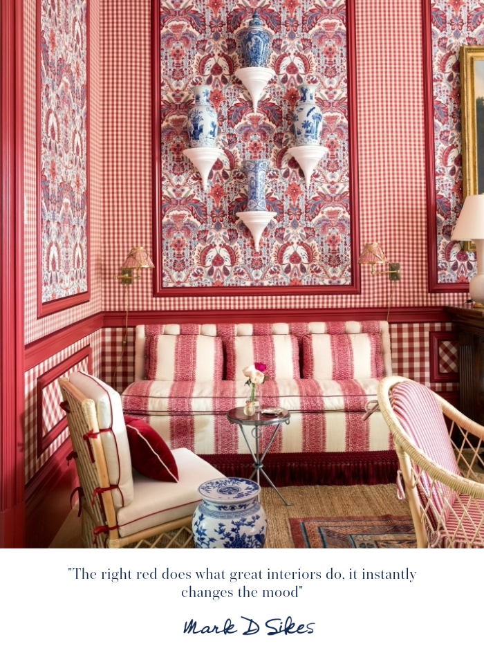 A red and white room with gingham and floral wallpaper, a striped sofa, and blue and white vases on shelves.