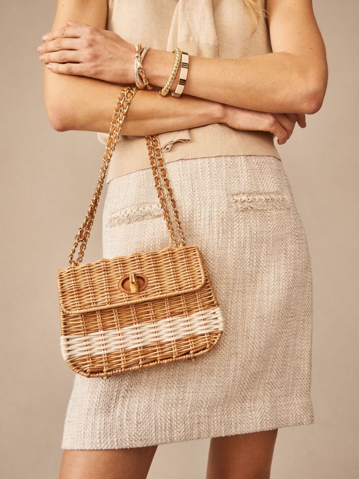 cropped image of woman wearing tan tweed skirt and holding a wicker bag with gold chain link strap