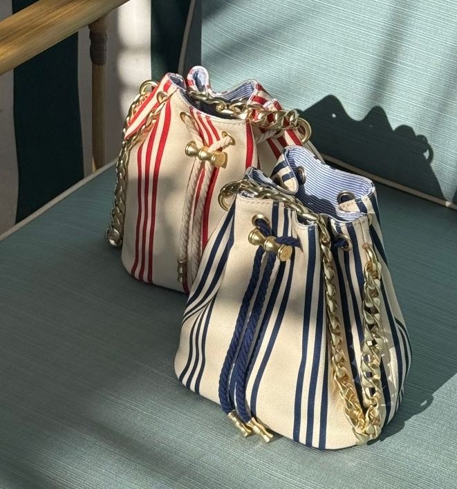 Two canvas bucket bags, one red-and-white striped and one navy-and-white striped, with gold chain straps.