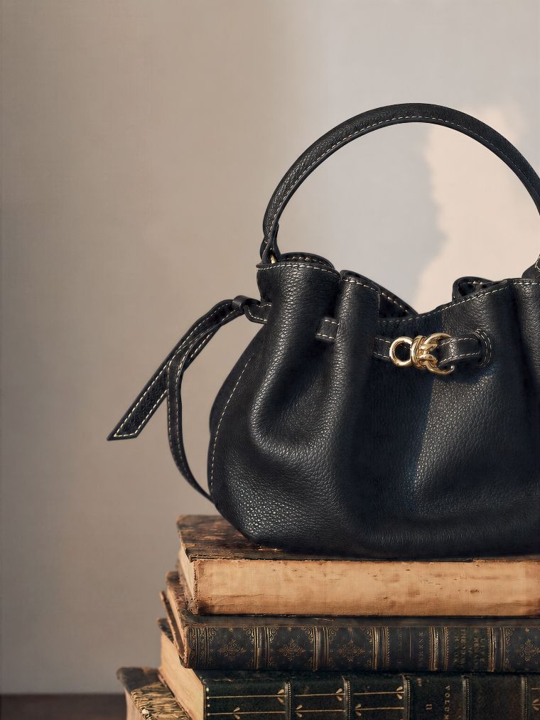Black pebbled leather bucket bag with white stitching and a gold clasp, on a stack of antique books.