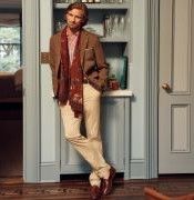 man leaning in dining room doorway wearing khaki pants and a brown houndstooth blazer