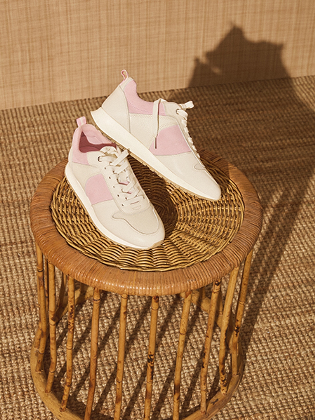 Pink and white women's sneakers posed on a wicker side table.