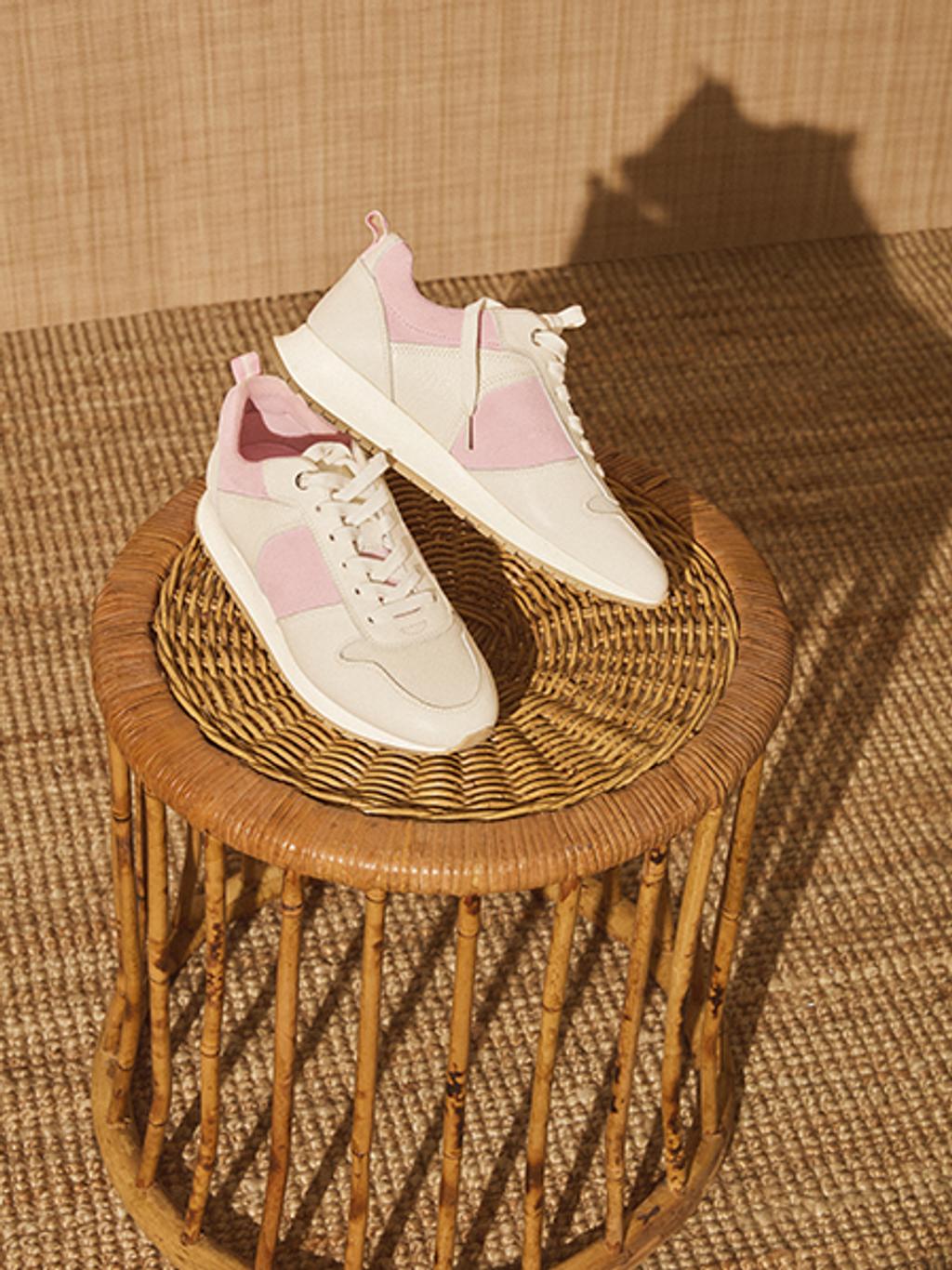 Pink and white women's sneakers posed on a wicker side table.