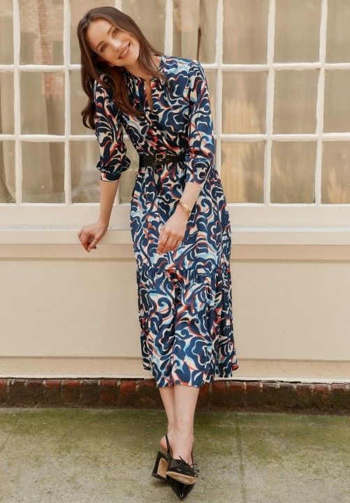woman standing outside against a window ledge wearing a blue geo swirl pattern midi length dress
