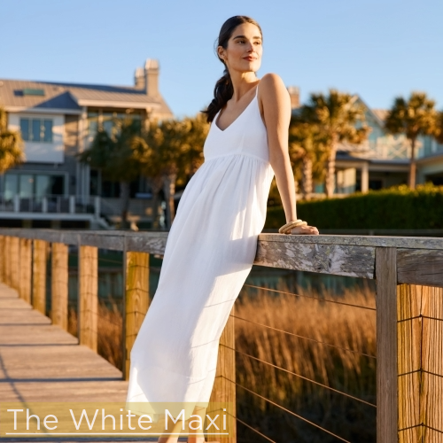 woman standing on pier with dunes and bay behind her wearing white spaghetti strap midi dress
