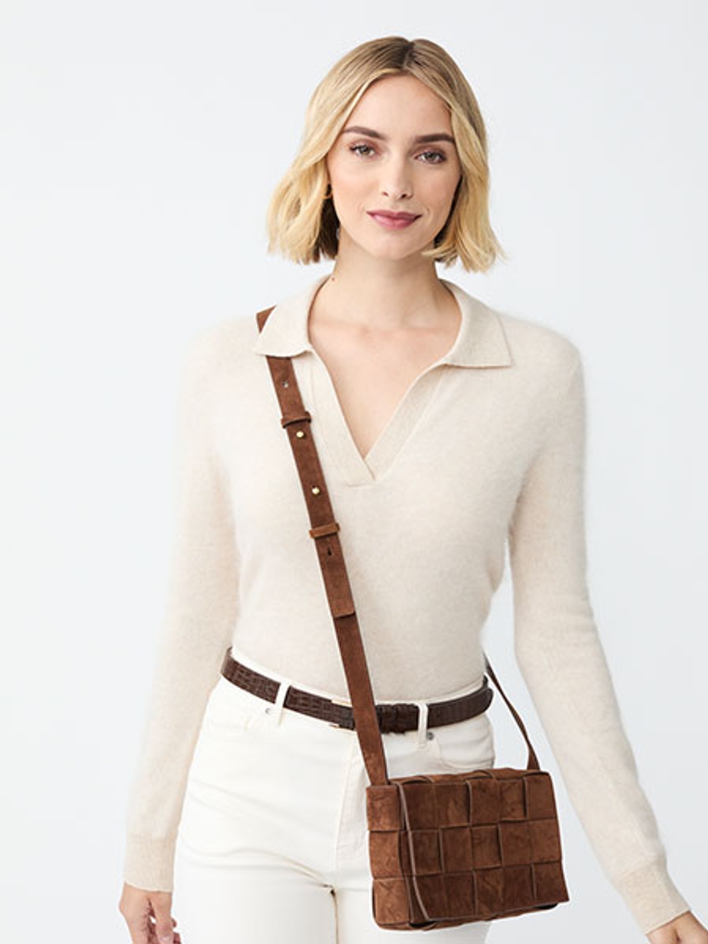 Model in a sweater and jeans wearing a woven crossbody bag Model in a sweater and jeans wearing a woven crossbody bag