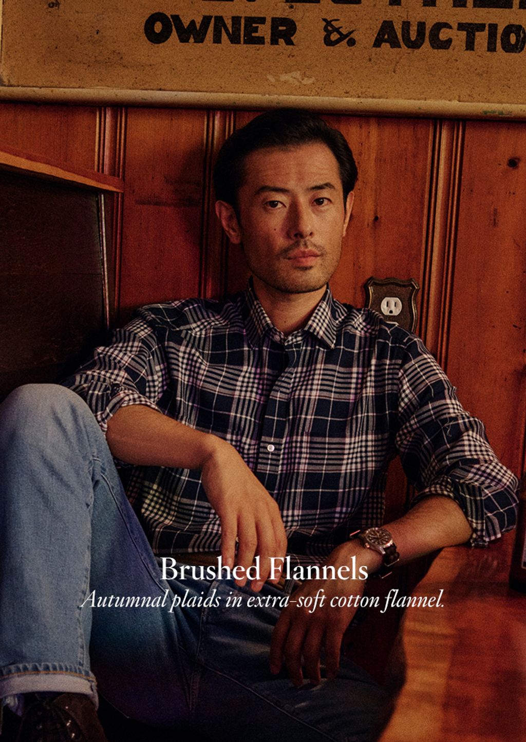 Man seated where a plaid flannel shirt and light wash jeans.