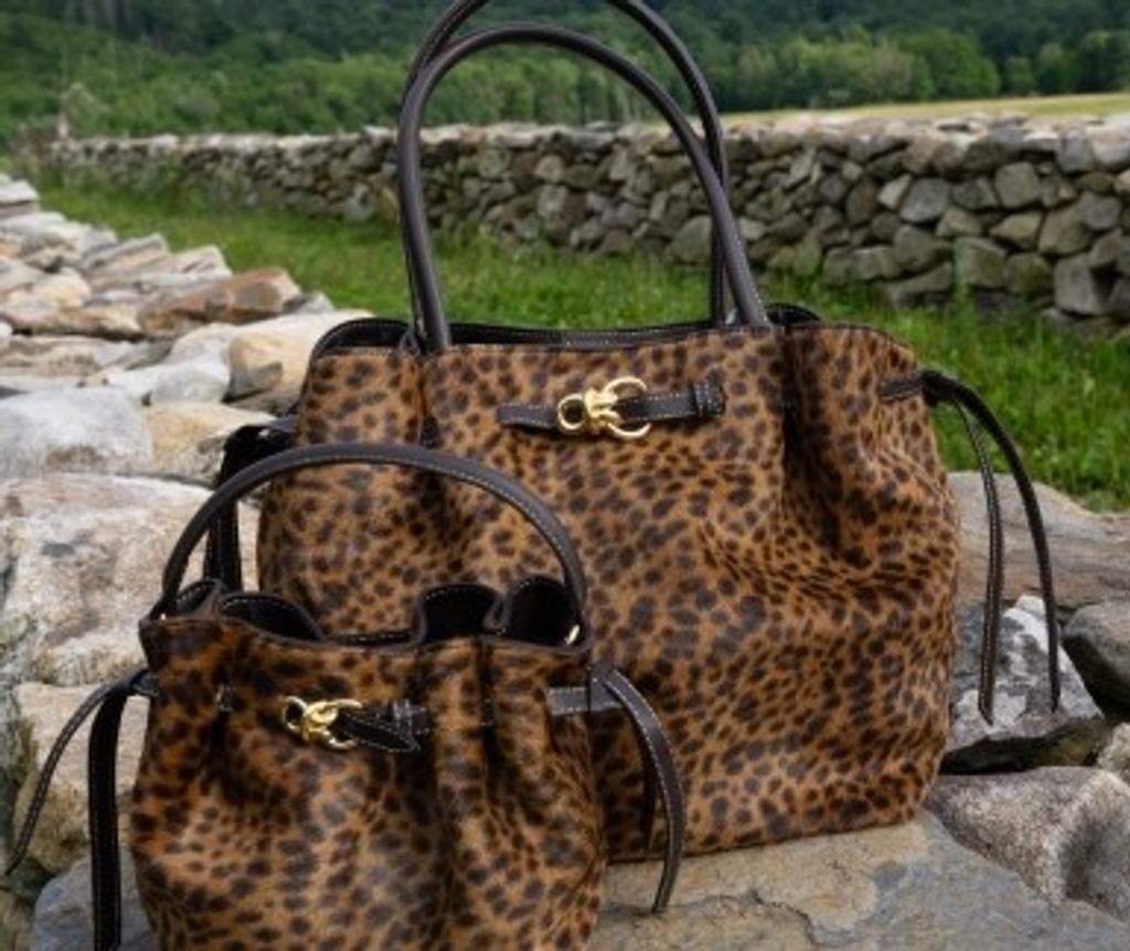Two matching leopard-print handbags on a stone wall.