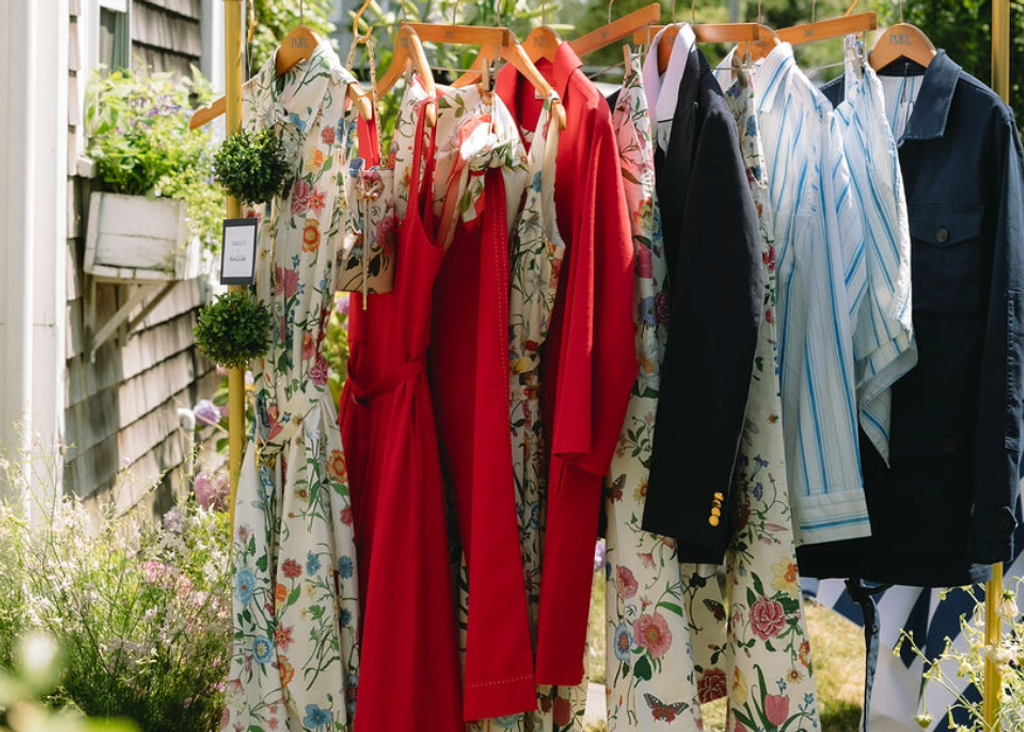 A rack of colorful clothing, including floral dresses, red dresses, a navy blazer, and striped shirts, displayed outdoors.