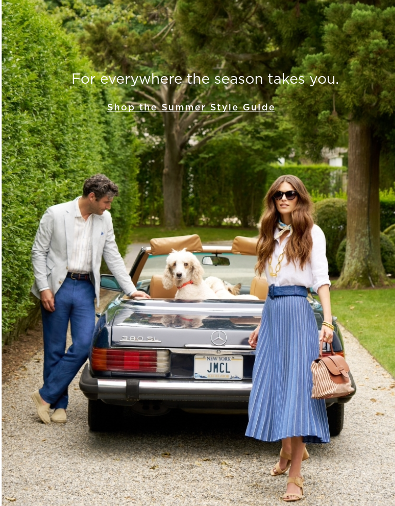 Woman seated on the top of a convertible, outside, wearing a navy pleated skirt with a white linen button down shirt tucked in
