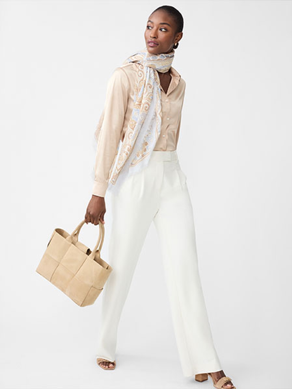 Women wearing white pants, tan button-down shirt, and a scarf holding a tan leather tote.