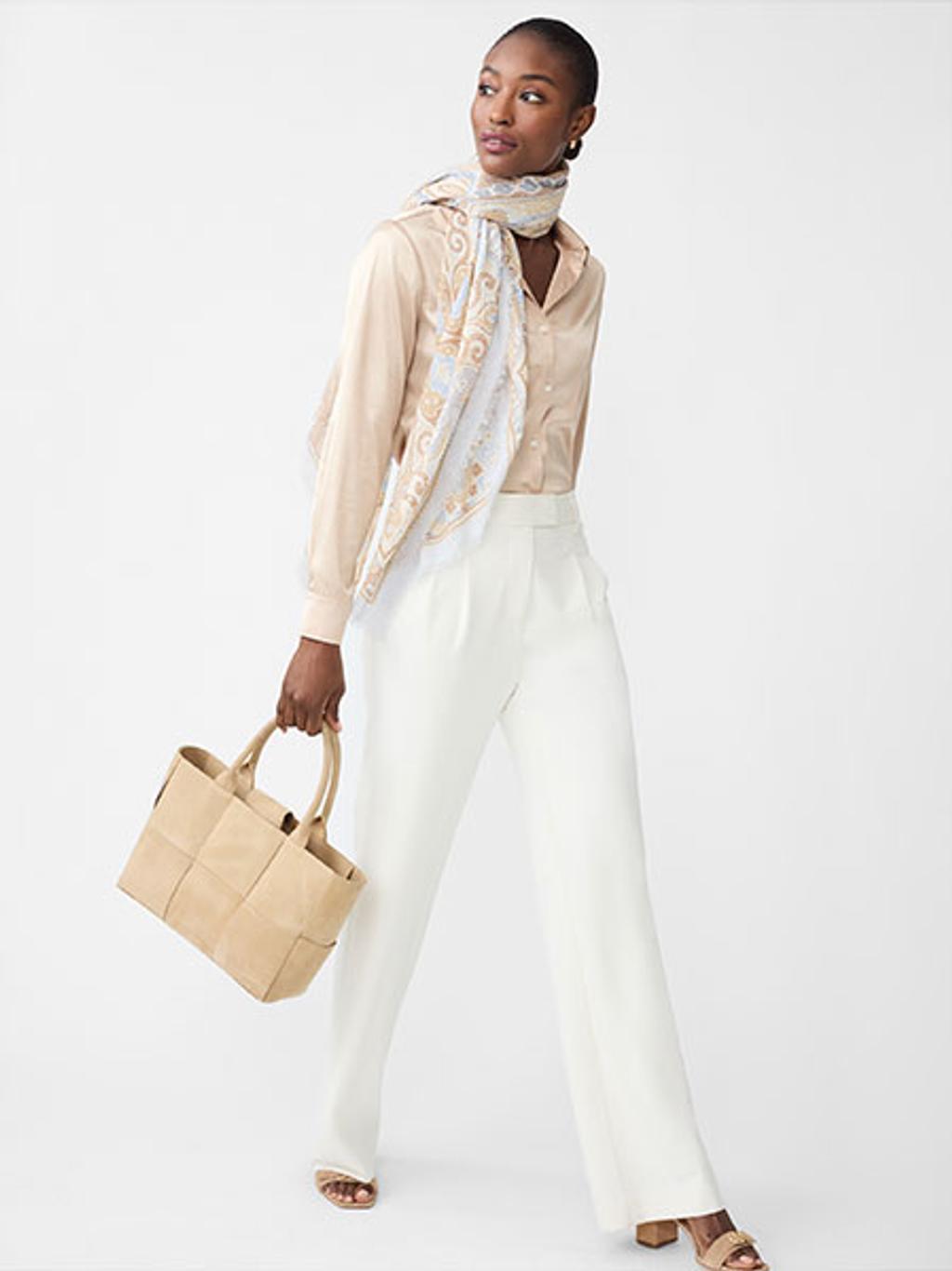 Women wearing white pants, tan button-down shirt, and a scarf holding a tan leather tote.