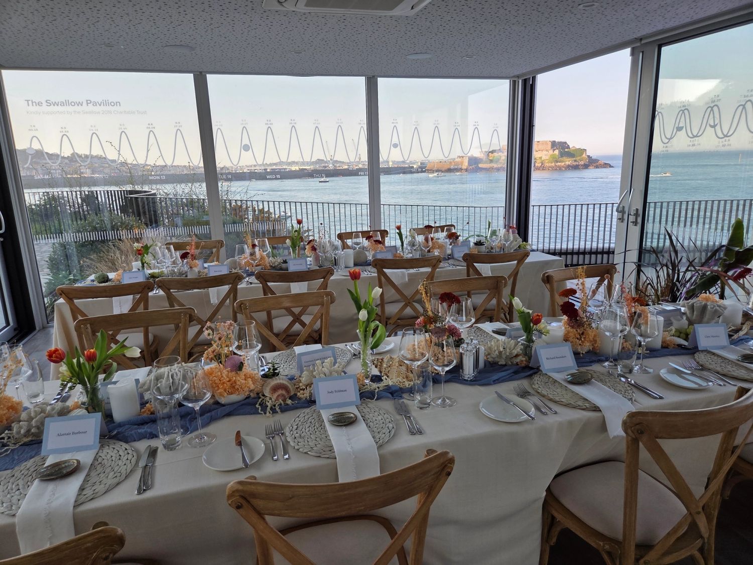 A long conference dinner table set beside floor-to-ceiling windows overlooking the sea