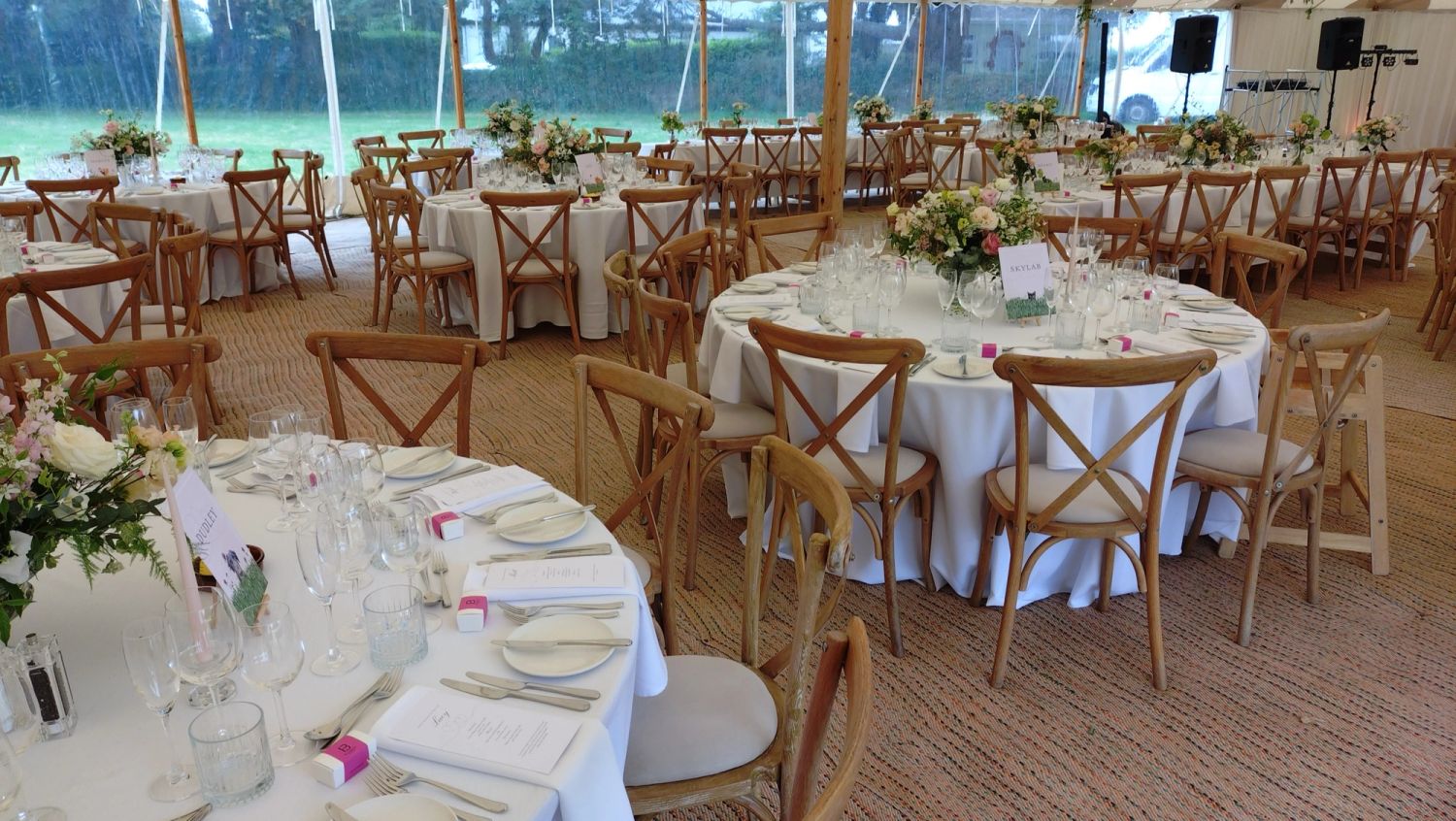 A wedding breakfast laid out under a marquee, round tables dressed with flowers and crossback chairs