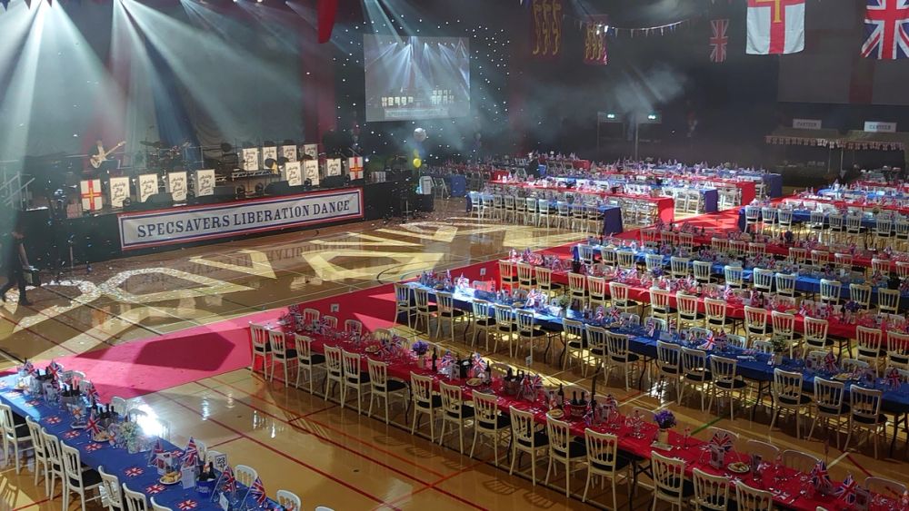 A grand ball with hundreds of guests seated at banqueting tables under stage lighting