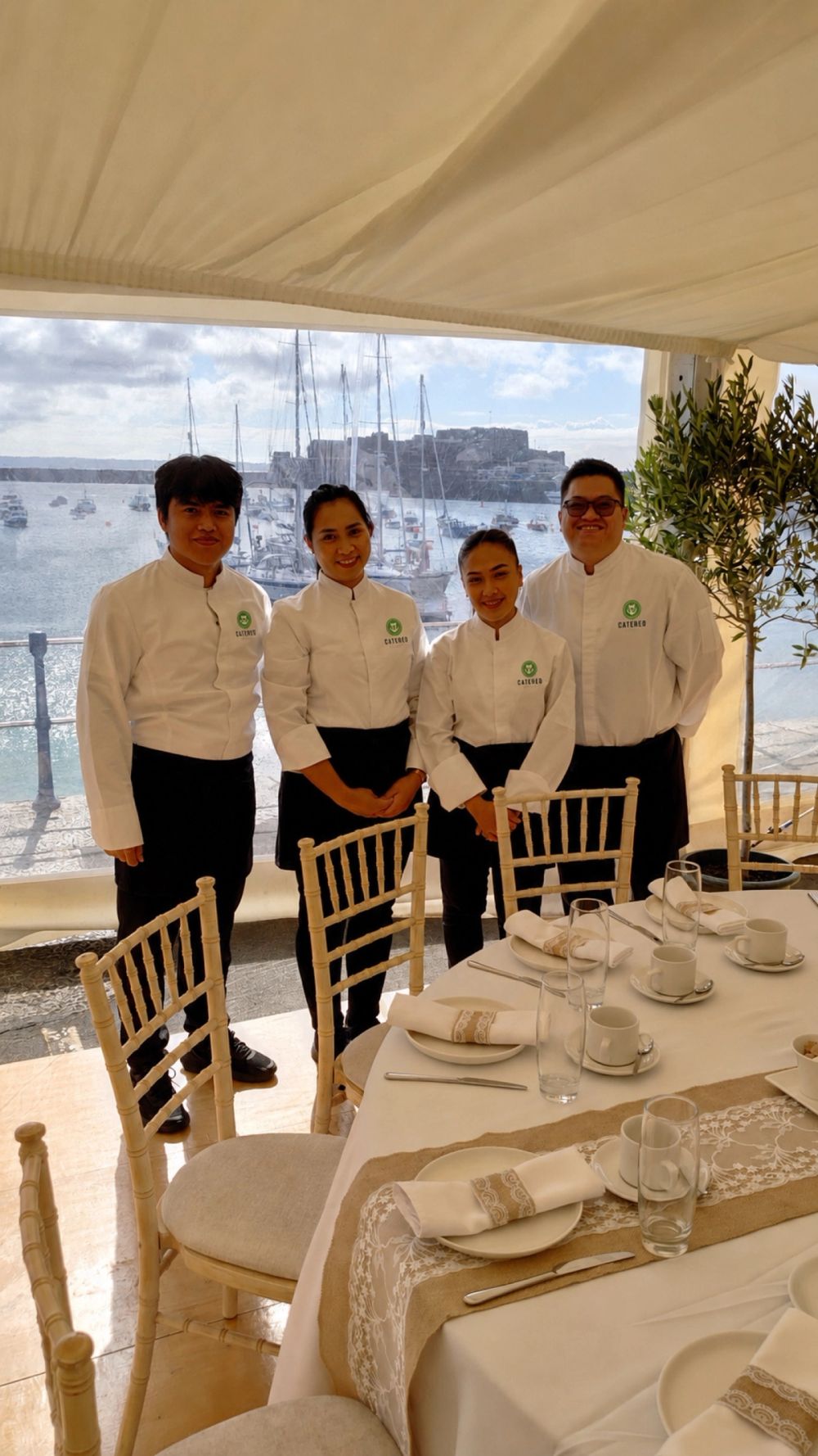 The Catered by Randalls team in branded whites beside a set table with the harbour behind them