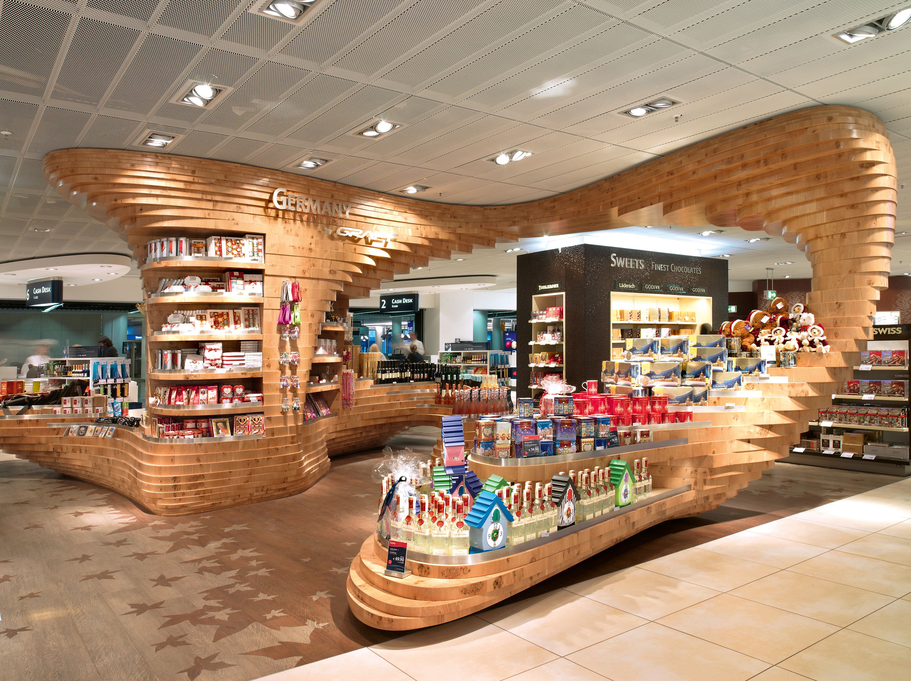 GRAFT designed forest-themed installations for the “Made in Germany” regional specialty areas of three different Heinemann duty free shops: Dynamic tree sculptures made of stacked layers of oak that serve as eye-catching centerpieces for shoppers.