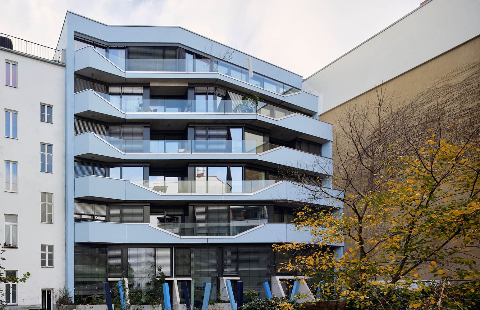 Moderner Wohngebäudekomplex mit großen Glasbalkonen und hellblauer Fassade, umgeben von älteren Gebäuden