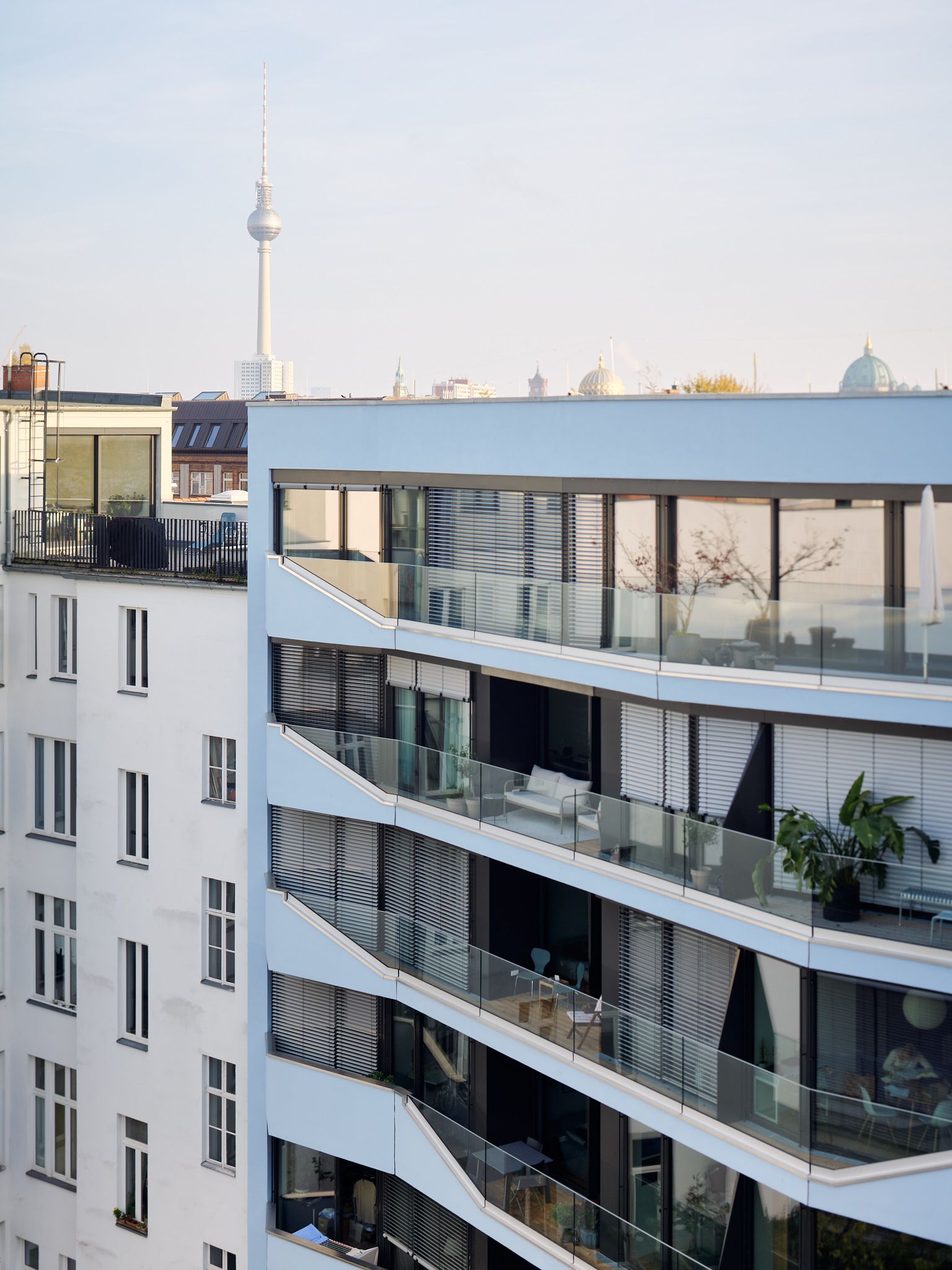 Moderner Wohnkomplex mit Balkonen und Glasgeländern, im Hintergrund der Berliner Fernsehturm bei klarem Himmel