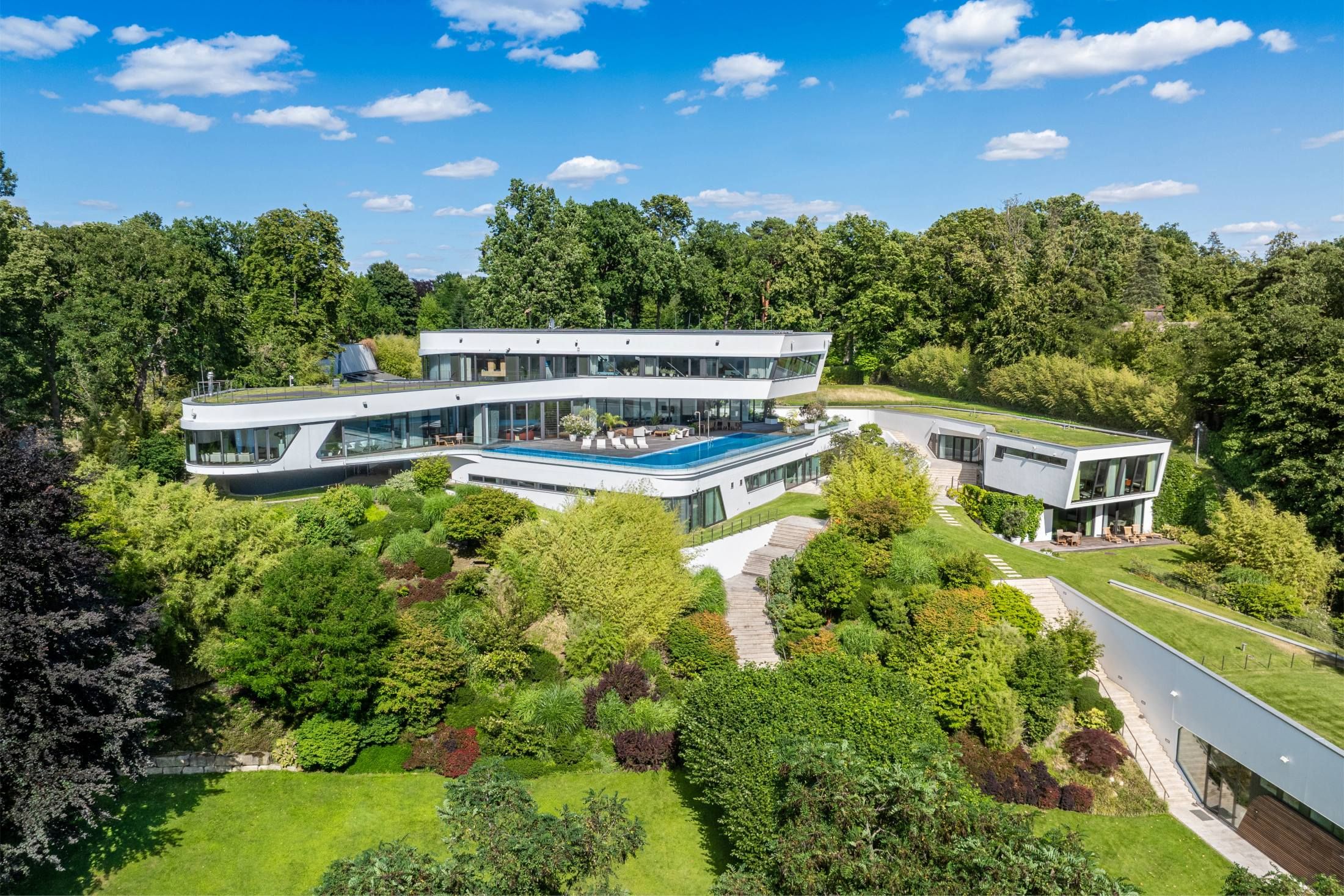 Großes modernes Wohnhaus mit mehrere, sich verschränkenden Bauteilen, umgeben von dichtem Grün und Gartenanlagen