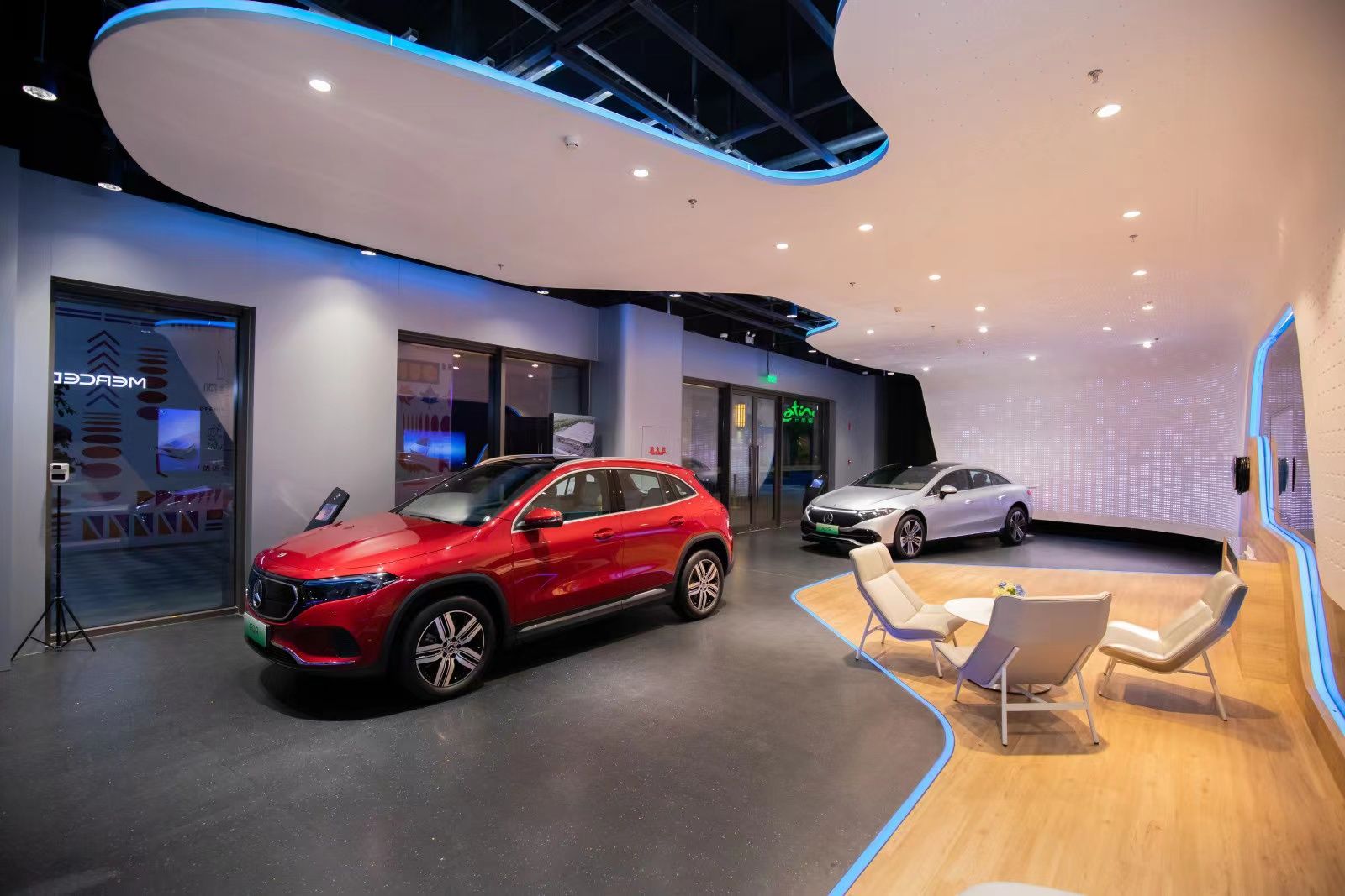 Innenraum eines modernen Autohauses mit zwei ausgestellten Autos und Sitzbereich mit Stühlen und Tisch