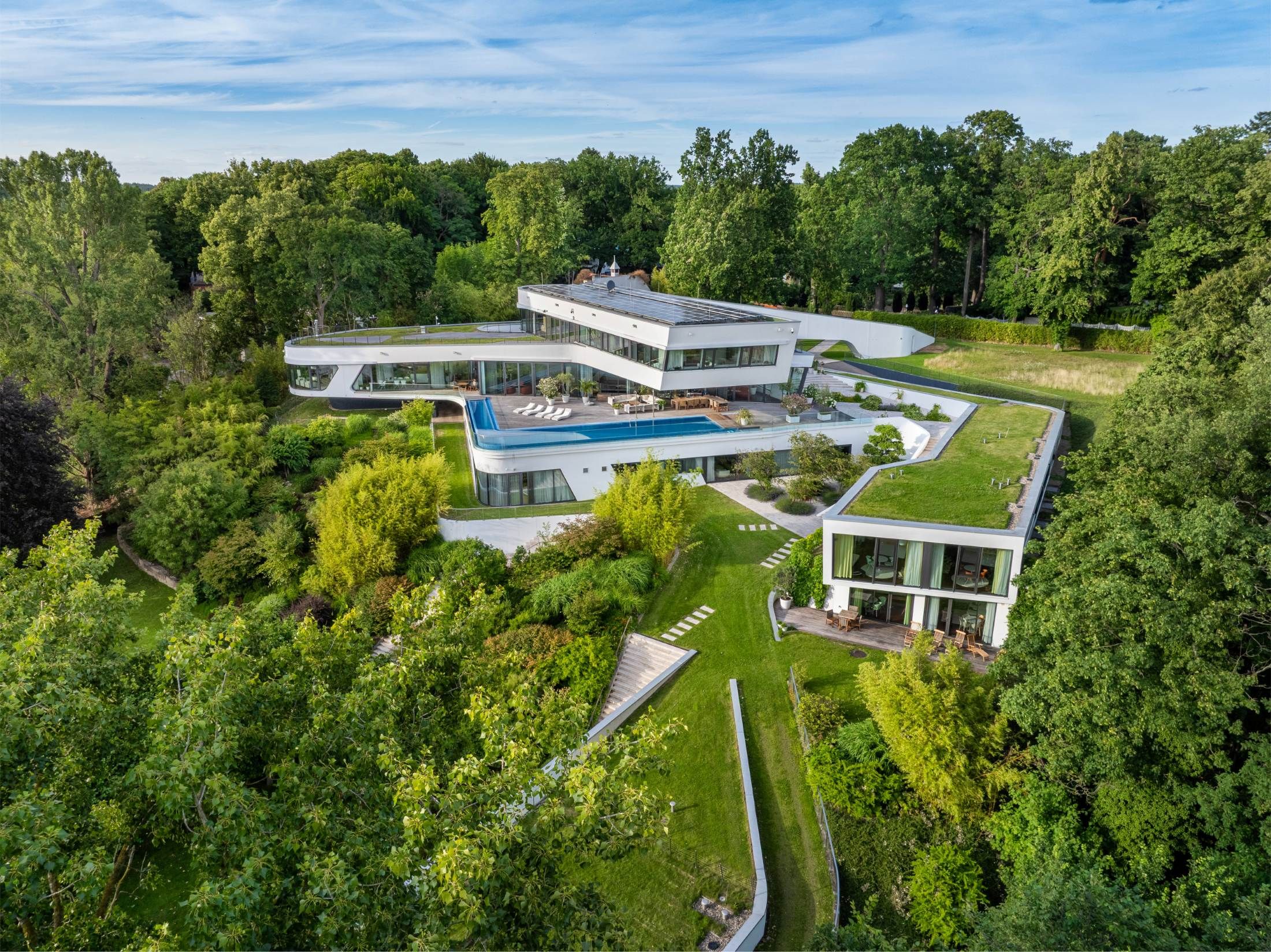 Großes modernes Wohnhaus mit mehrere, sich verschränkenden Bauteilen, umgeben von dichtem Grün und Gartenanlagen