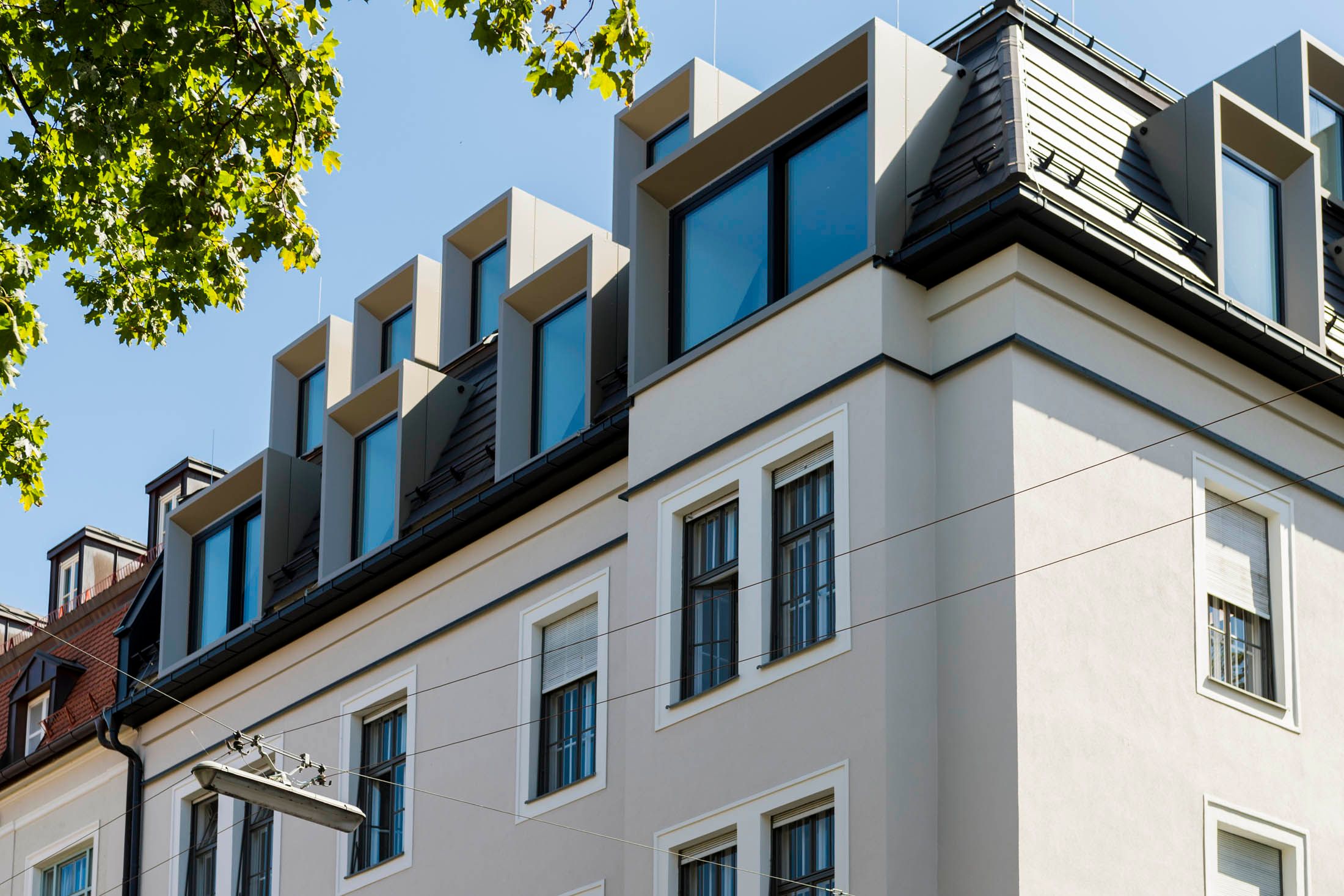 Eckansicht eines mehrstöckigen Wohngebäudes mit modernen Dachgauben und weißen Fassaden unter blauem Himmel