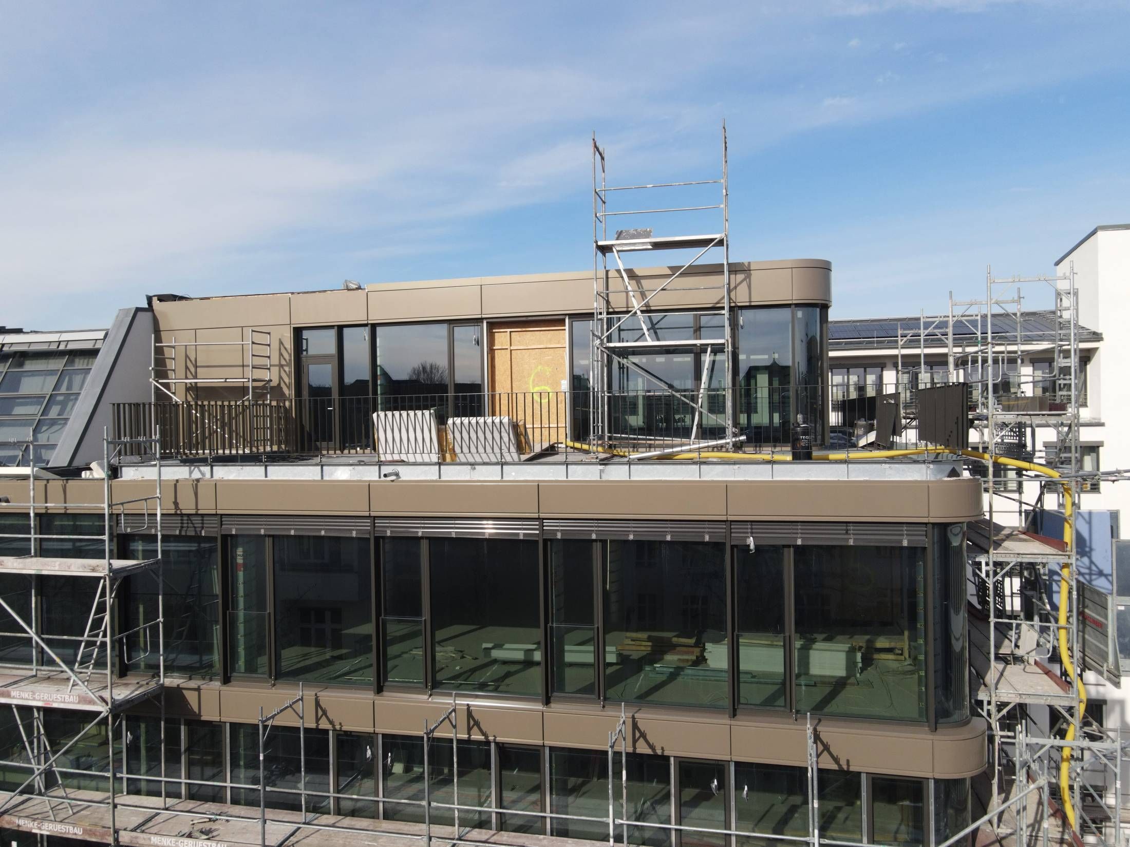 Mehrstöckiges modernes Gebäude mit großen Glasfenstern und Gerüst an der Fassade bei klarem Himmel