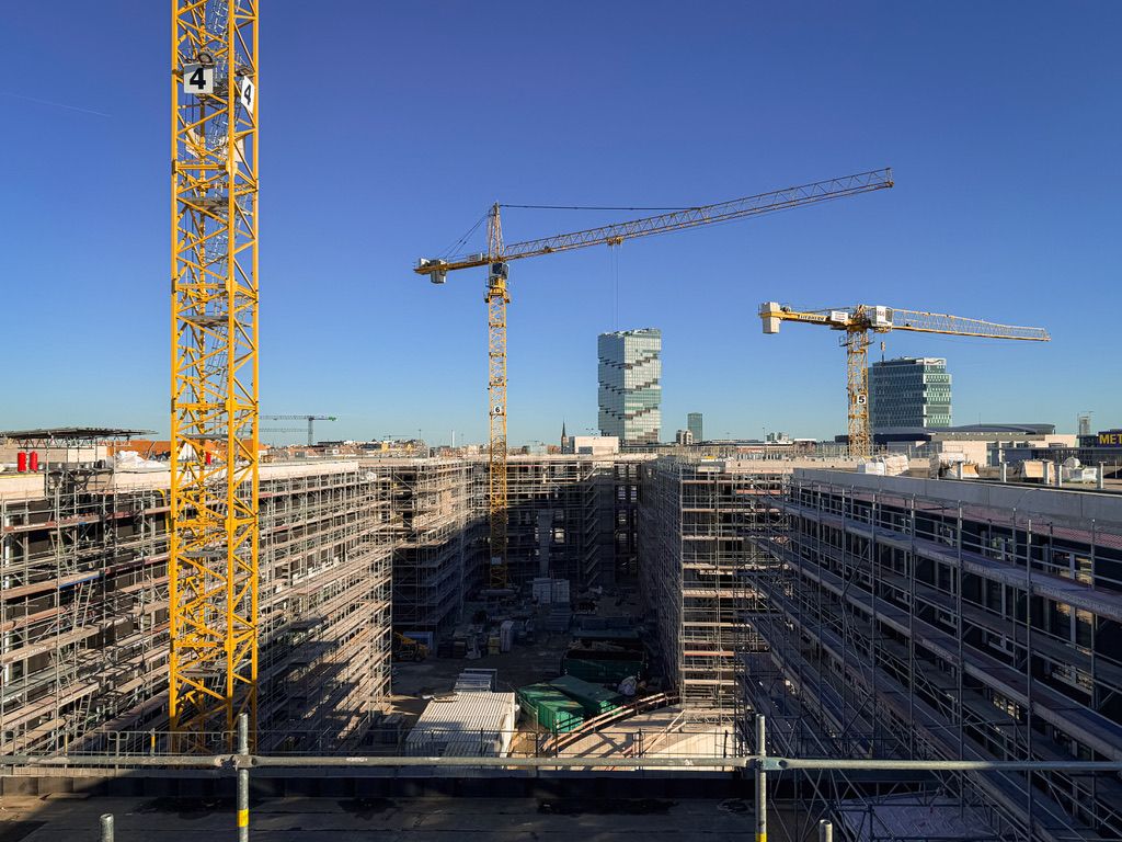Baukräne über einer großen Baustelle mit mehrstöckigen Gerüsten unter klarem Himmel