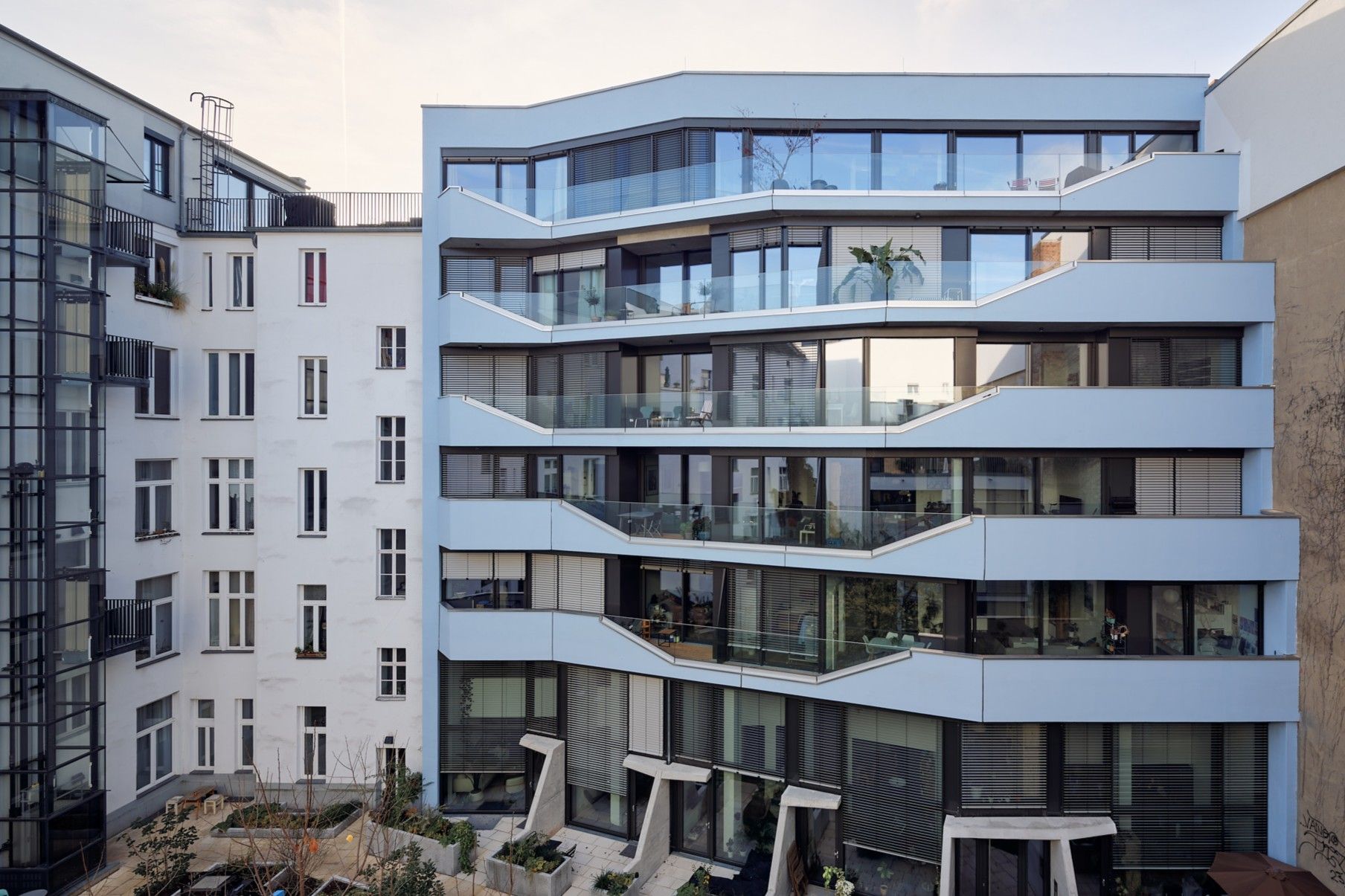 Moderner Wohngebäudekomplex mit großen Glasbalkonen und hellblauer Fassade, umgeben von älteren Gebäuden