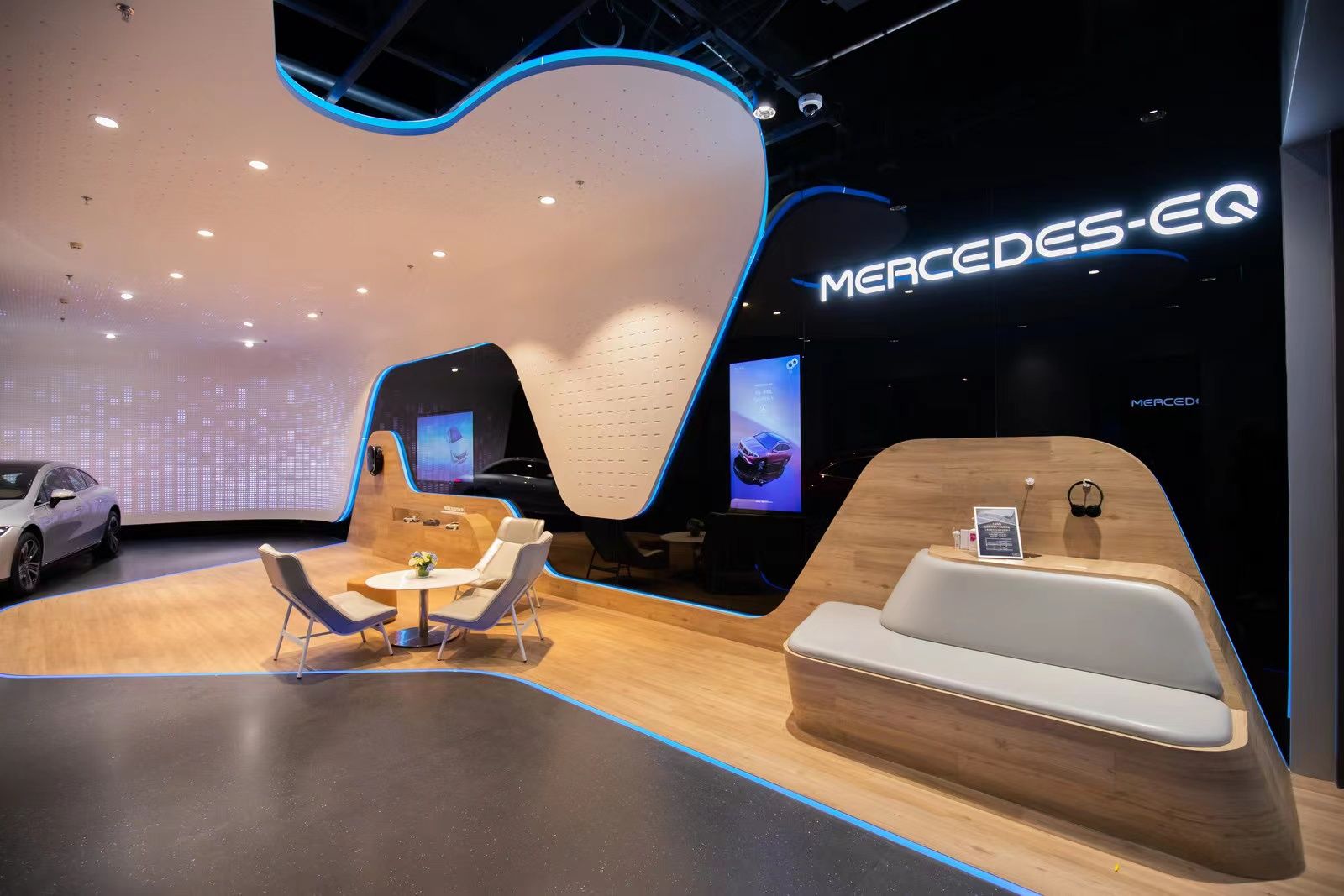 Modern showroom with seating area, wood paneling, and illuminated 'MERCEDES-EQ' sign on black wall