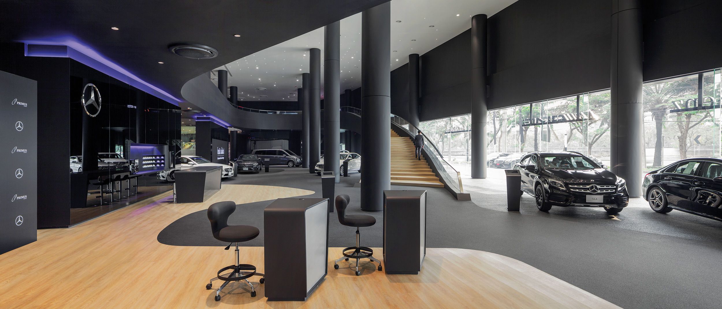 Interior of a modern car dealership with several displayed cars, seating areas, and a staircase in the background