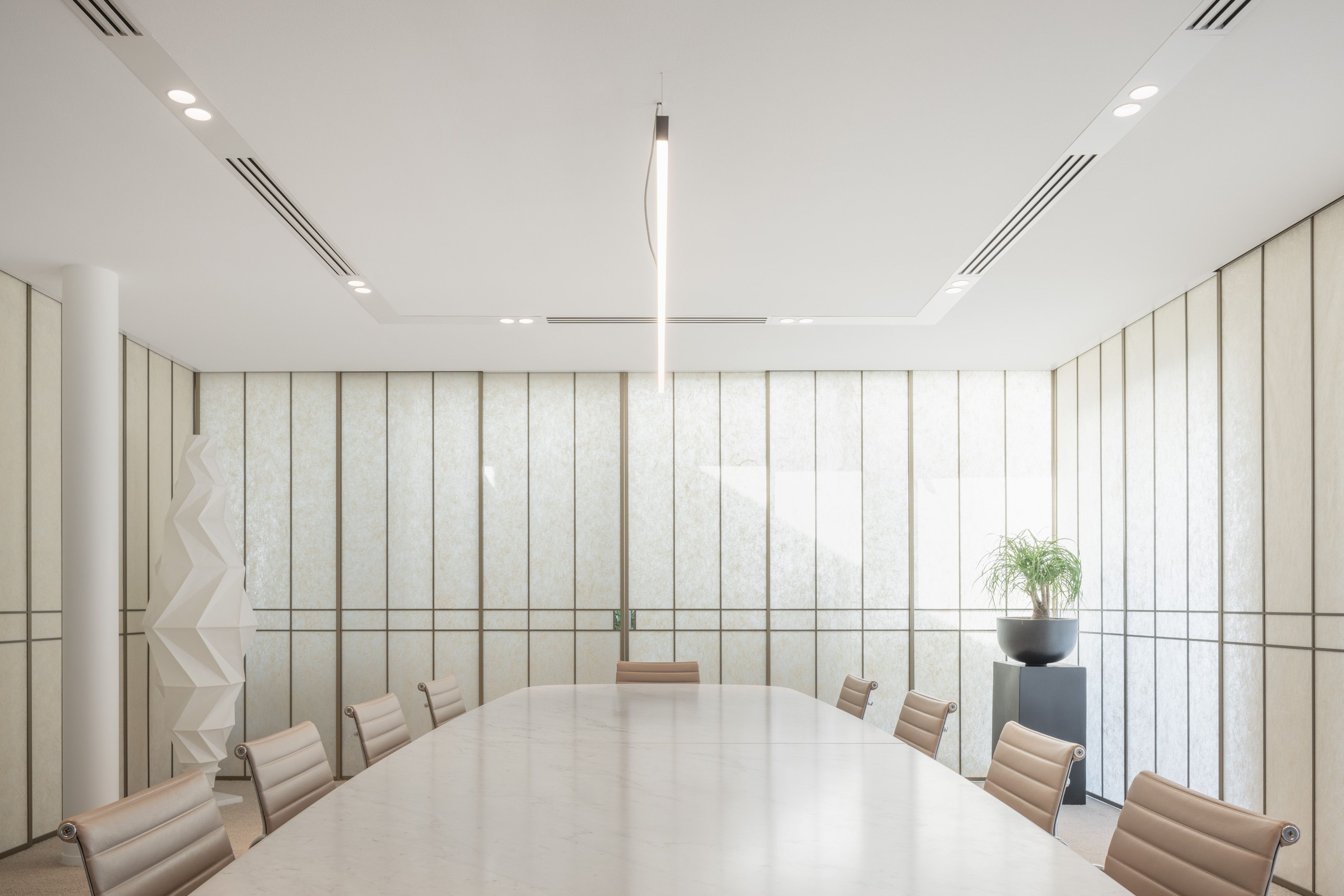 Modern conference room with a long white marble table, eight beige leather chairs, vertical panel walls