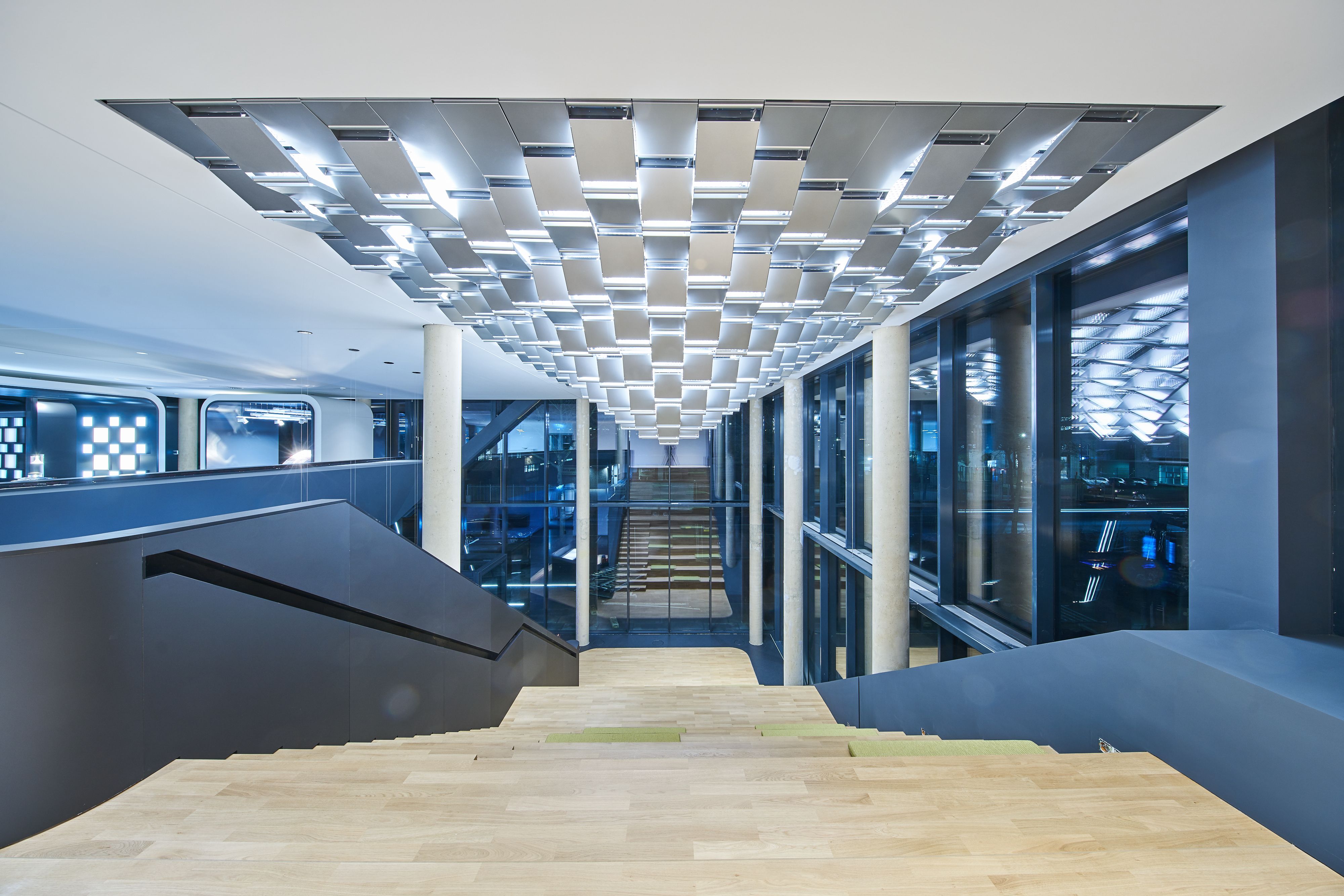 TRILUX LIGHT CAMPUS Project type: Office Building     Location: Cologne, Germany     Client: Trilux GmbH & Co KG     Time: 2017-2019     Size: 2,794m2     Photos: Trilux  GRAFT designed the new campus of the German lighting company TRILUX in Cologne. The design of the rectangular building is strongly inspired by the client’s craft: light, refraction and reflections are reflected – in the truest sense of the word – throughout the building and its design embodies the precision of lamp manufacture. The continuous, staggered glass façade presents a changing pattern of reflections from different viewpoints and draws inspiration from the aesthetics of spotlight reflectors, which optimize the optical distribution of the light source. To achieve this, each façade module is rotated at the same angle about its central axis. The overall impression is of a monolithic building that produces different light and depth effects depending on the point of view.
