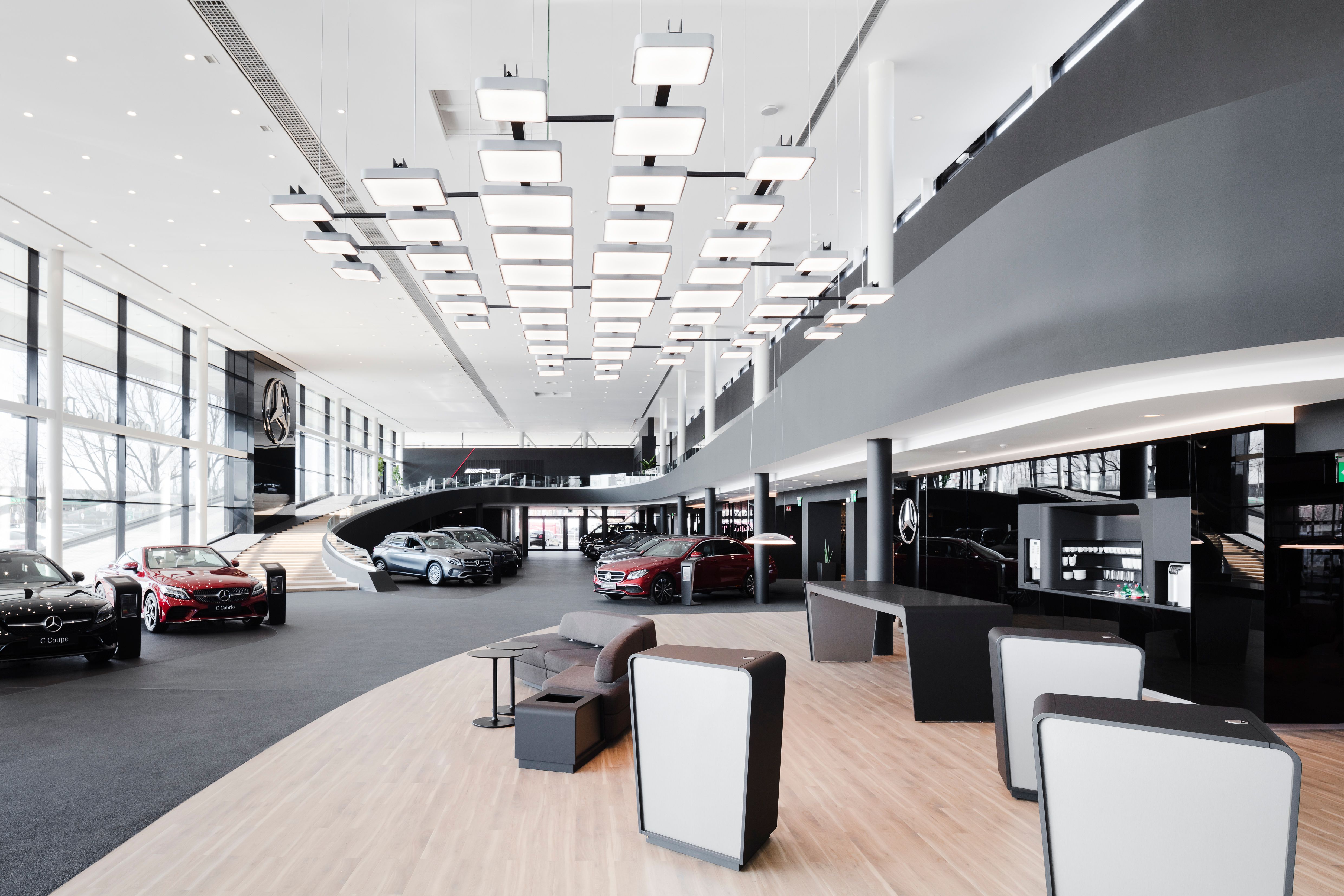 car showroom featuring several luxury vehicles, bright ceiling lights, and a reception desk. Black and white color scheme.