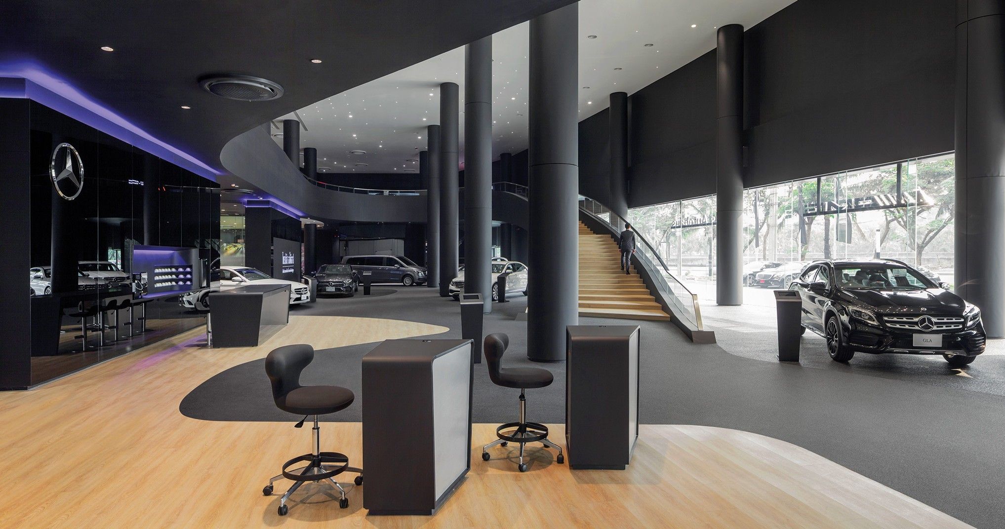 Interior of a modern Mercedes-Benz dealership with cars, seating areas, and a staircase