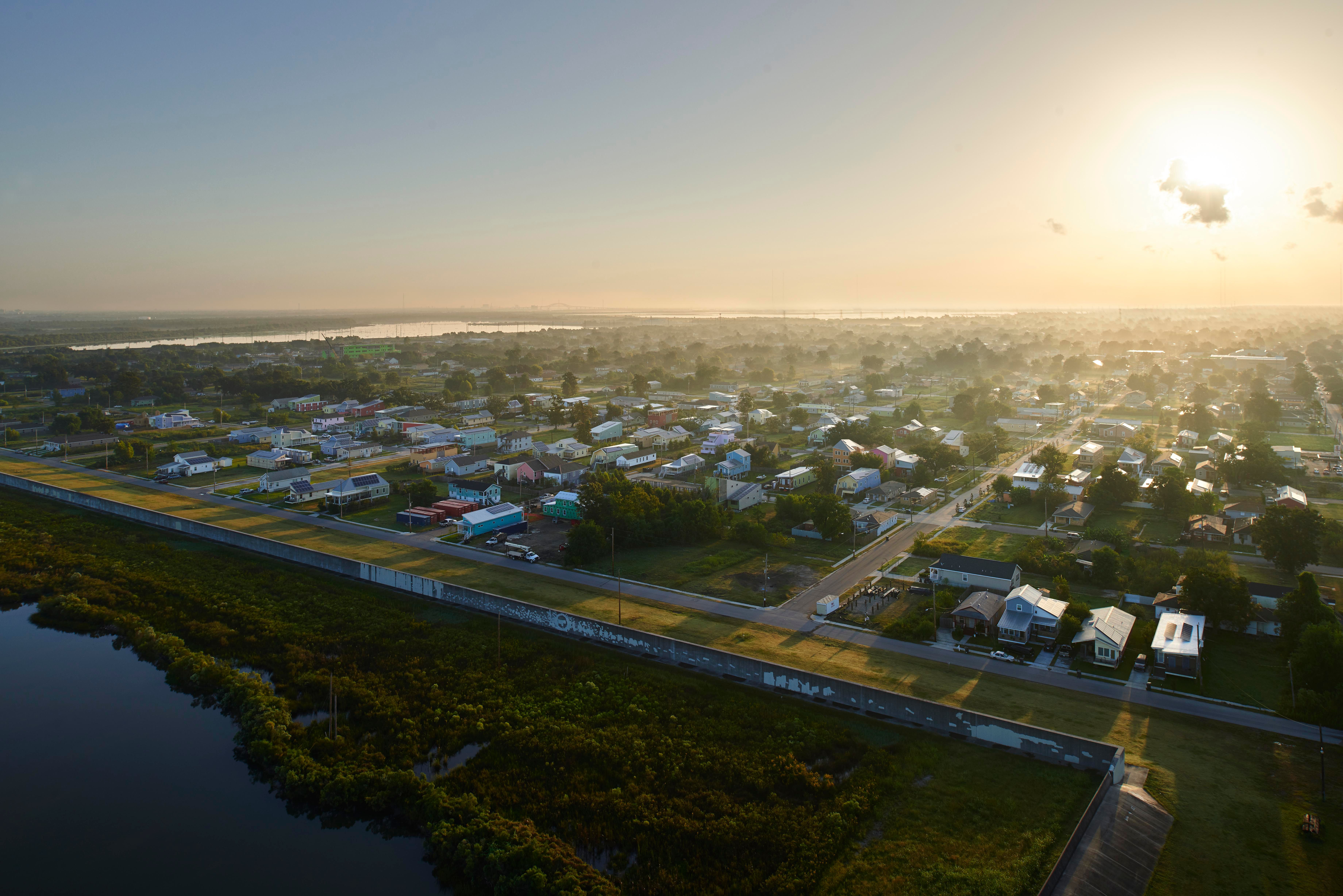 Aerial view of New Orleans with small houses and streets at sunset, bordered by a waterway and green vegetation.