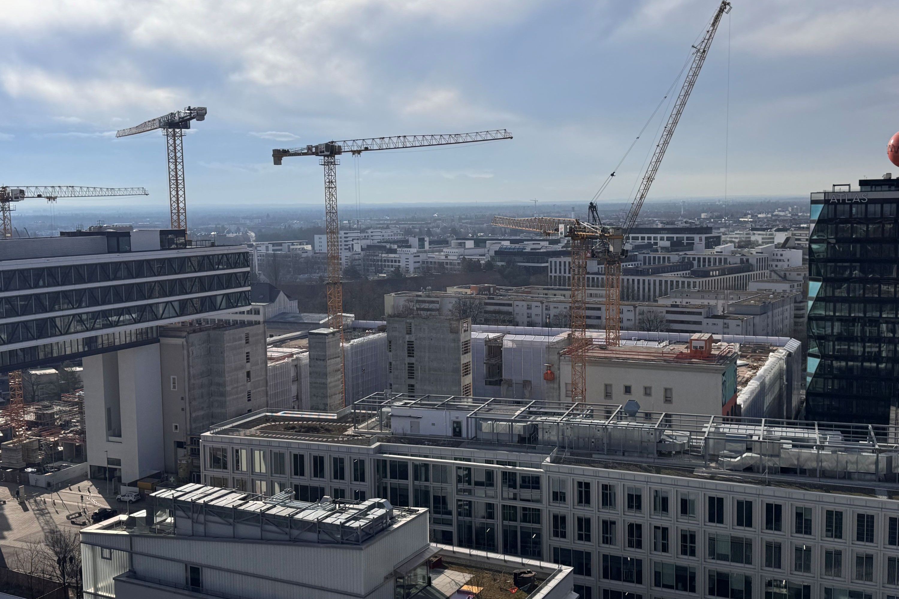 View over a city with multiple construction cranes and multi-story buildings under a cloudy sky
