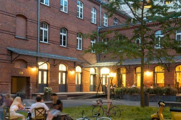 People sitting at outdoor tables in front of a brick building with lit windows and bicycles parked nearby
