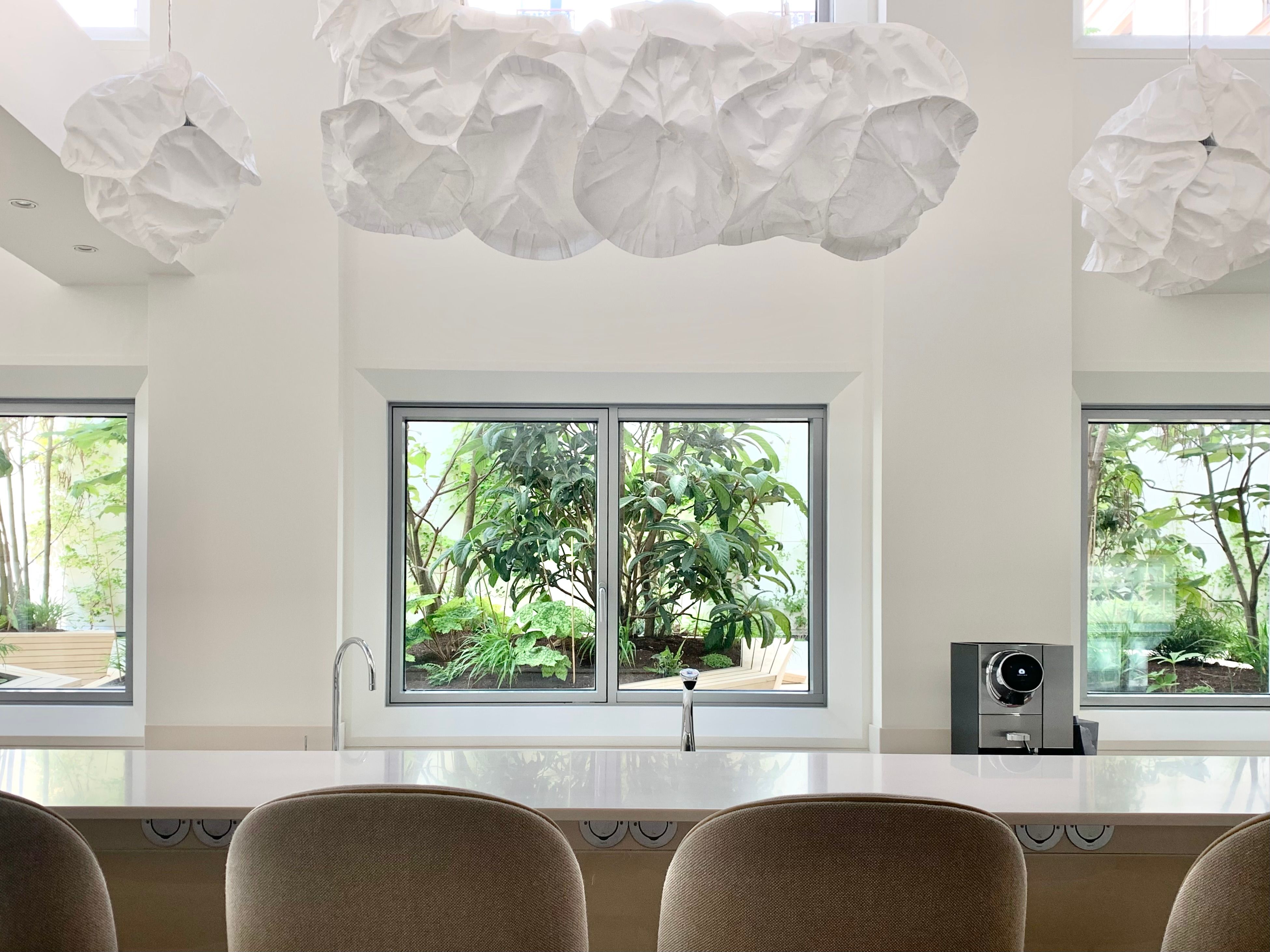 a white interior space with cloud-shaped pendant lighting. Windows in the background showing a lush green courtyard