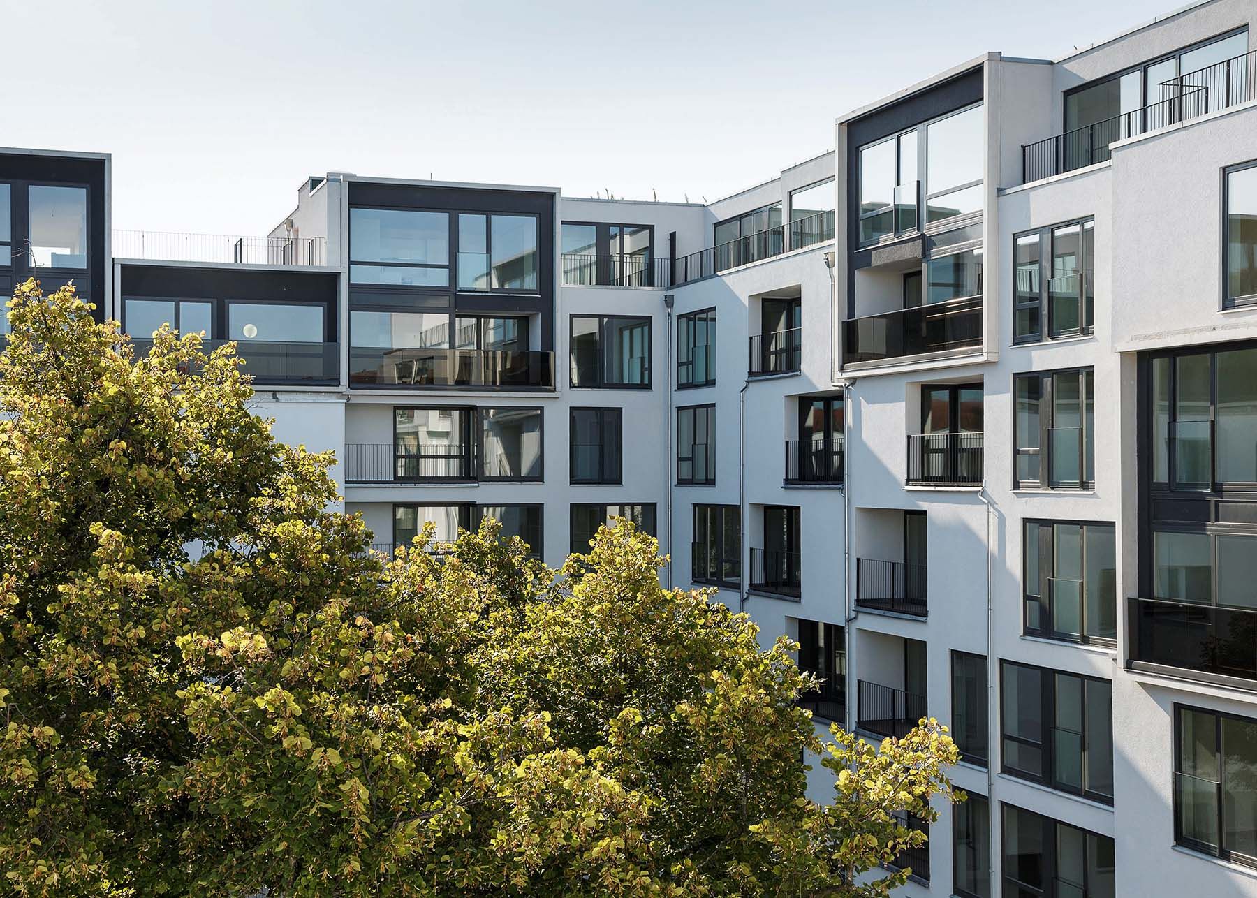 Modern multi-story apartment buildings with balconies behind leafy trees