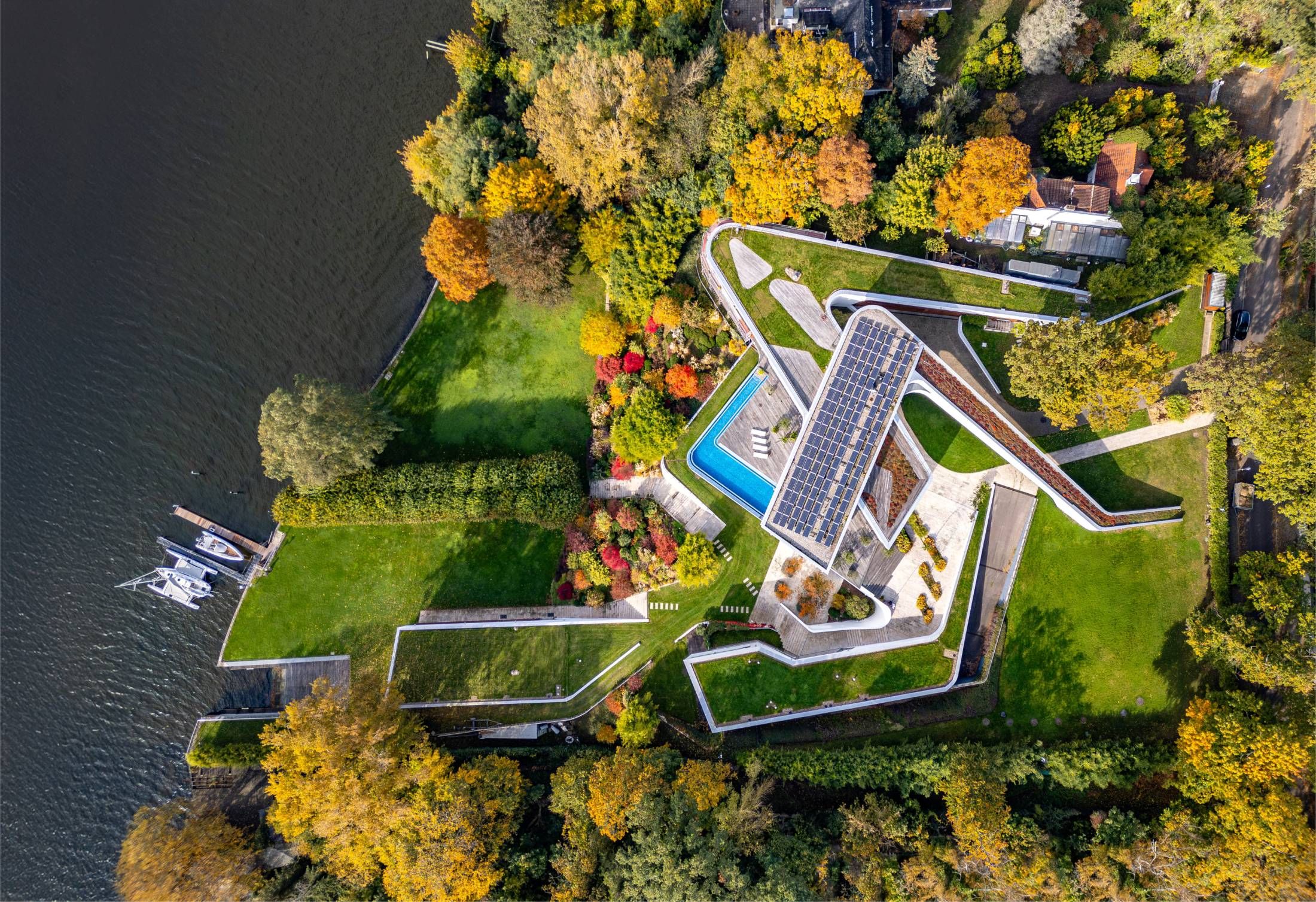 Aerial view of a modern building with overlaping building sections, a green roof and solar panels by a body of water
