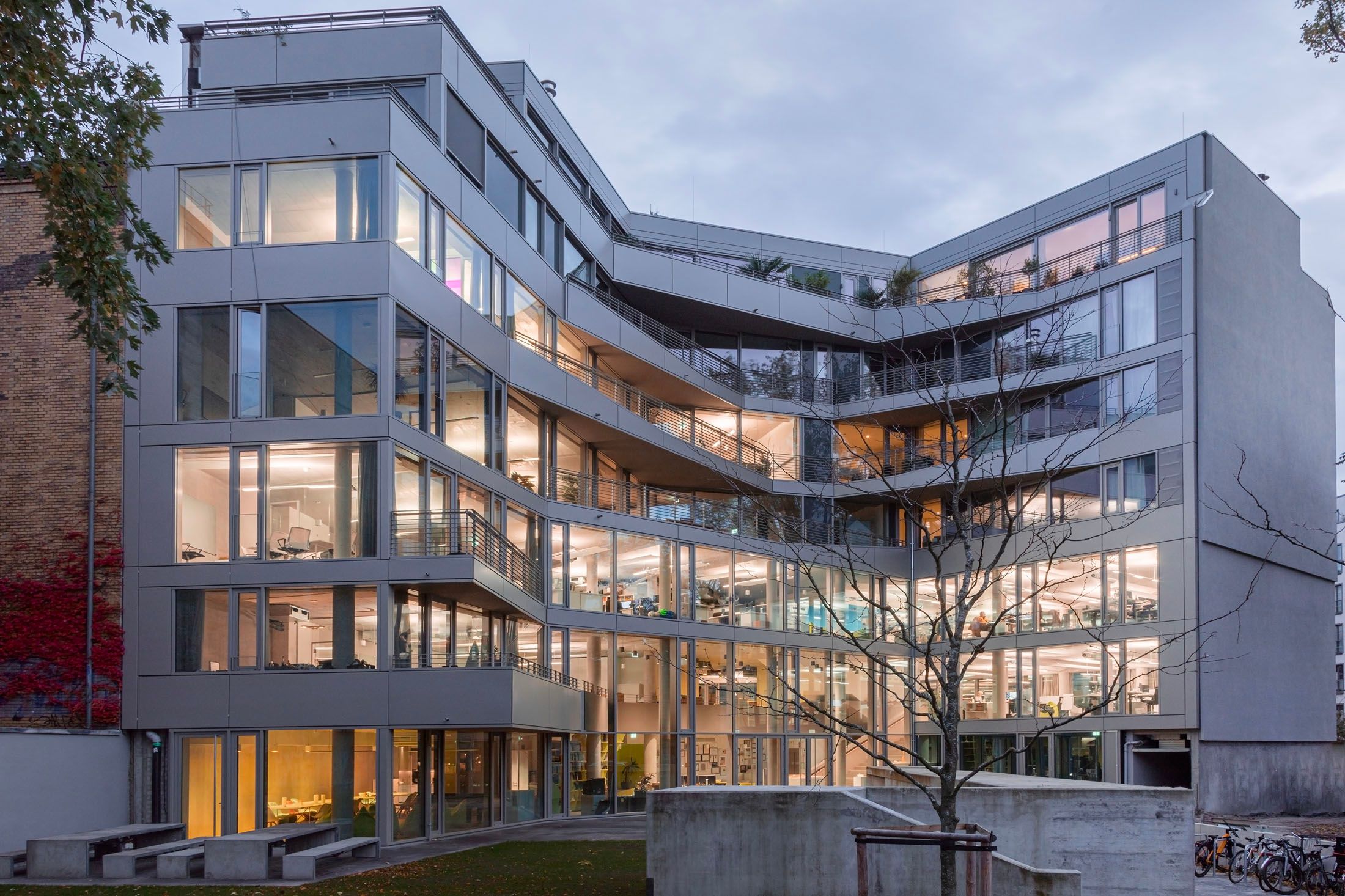 Modern multi-story office building with large glass windows and a courtyard with a leafless tree