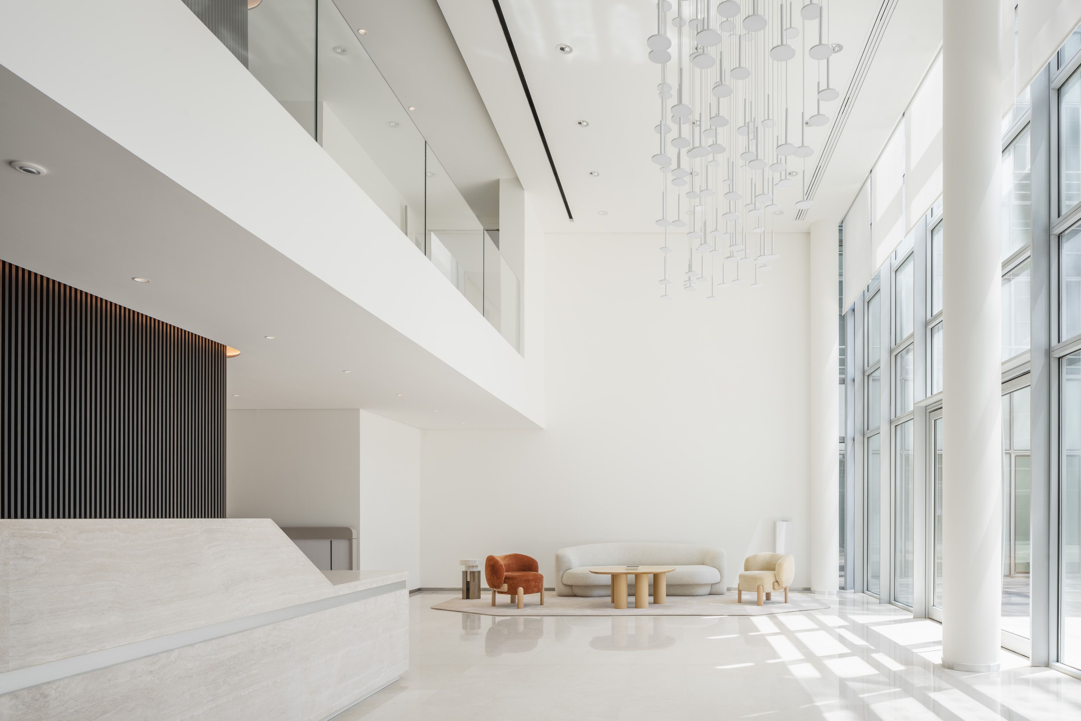Spacious modern lobby with high ceiling, large windows, white walls, beige floor, a white sofa