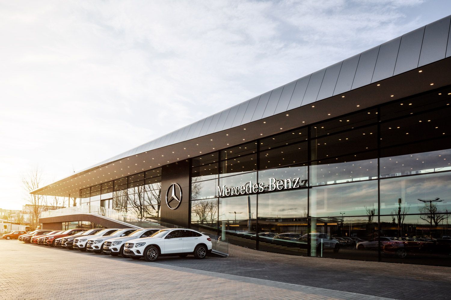 Modern Mercedes-Benz dealership with glass facade and multiple cars parked in front