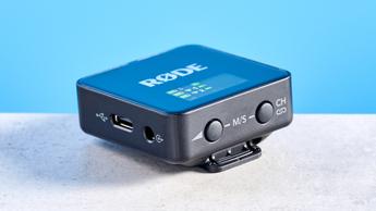 Das Rode Wireless GO Gen 3 Mikrofon-System mit einem Empfänger und zwei Sendern, präsentiert auf blauem Hintergrund mit Zubehör wie Windschutz, Ladeanschlüssen und Audiokabeln.