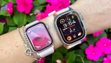 Nærbillede af en persons håndled med Apple Watch Series 10 og Ultra 2, med lyserøde blomster i baggrunden